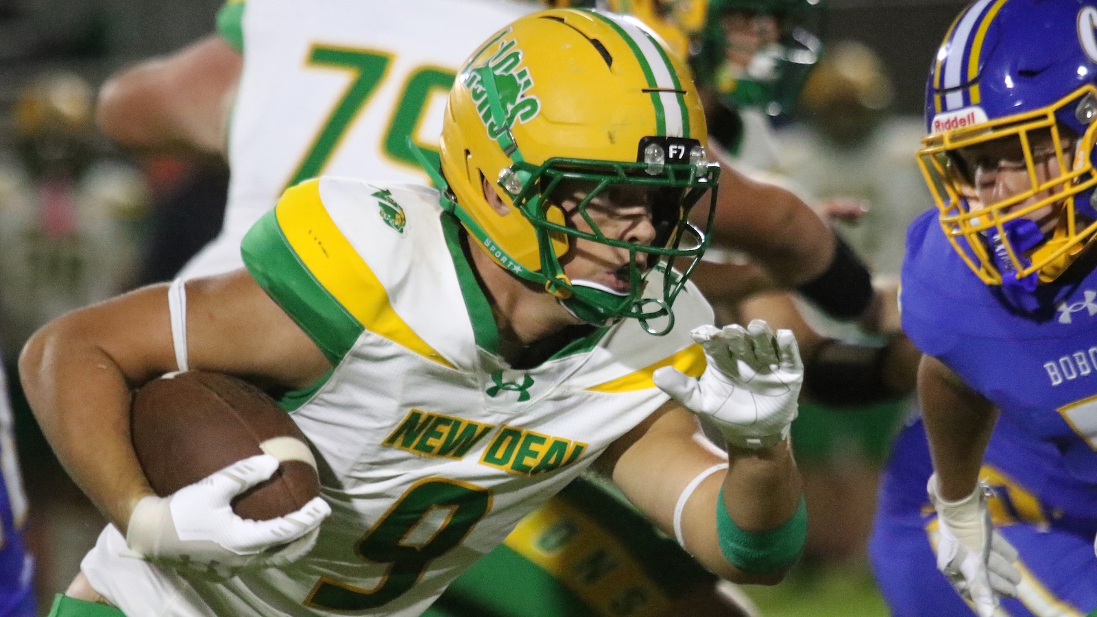 Football player in a white-green-yellow New Orleans jersey carries the ball, sprinting forward as a defender in purple closes in.