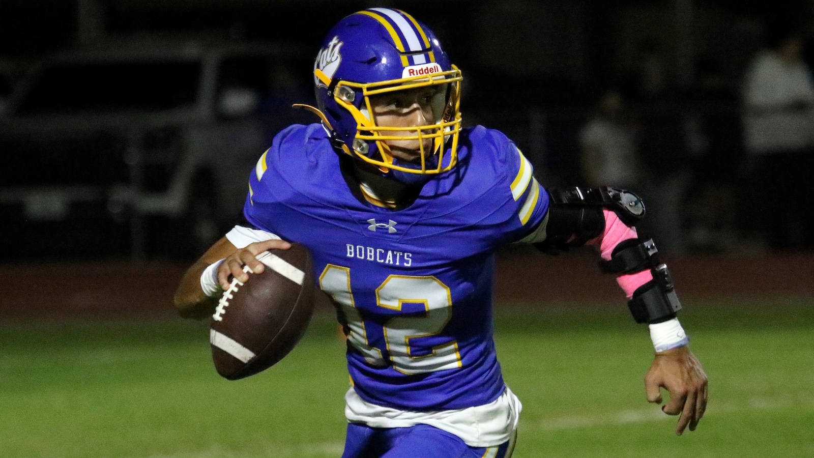Bobcats football player in blue and gold jersey runs with the ball on a night game field.