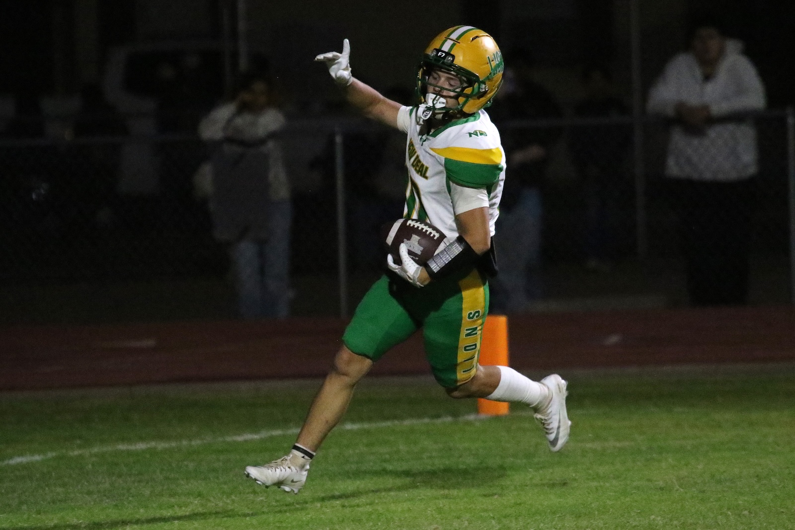 Football player in green and yellow uniform runs with the ball during a night game, arm raised in celebration or signal