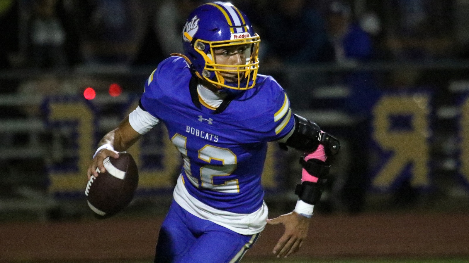 Bobcats football player in blue and gold (No. 12) runs with the ball during a night game.