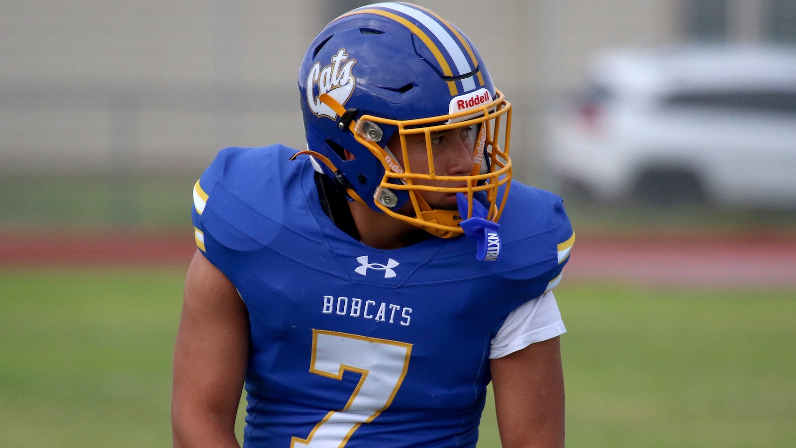 American football player in a blue Bobcats uniform with number 7 and a yellow facemask helmet on the field