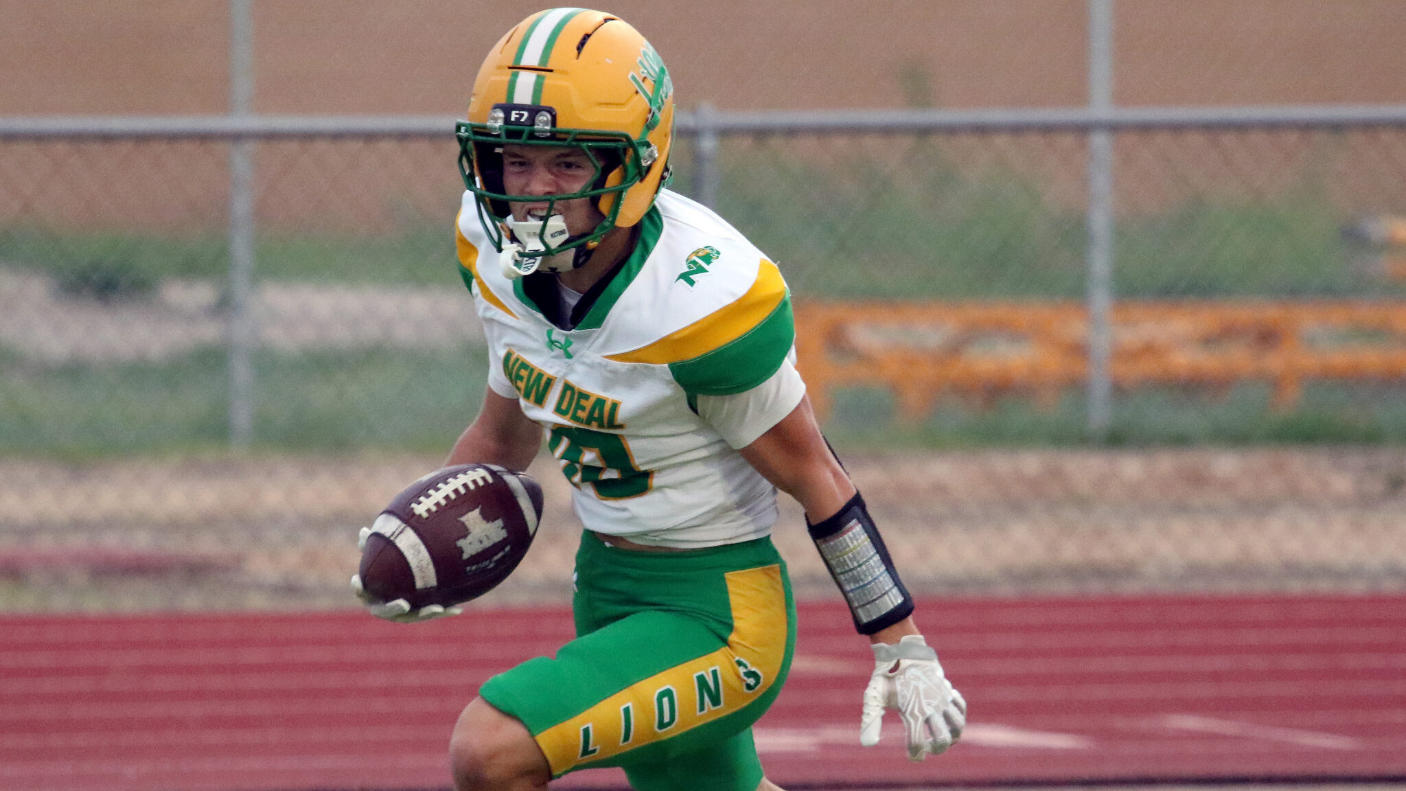 100326 - New Deal vs Sunray - Jacobi Creek | Press Pass Sports Football player in green and gold uniform runs with the ball on a track field ground surface in action.
