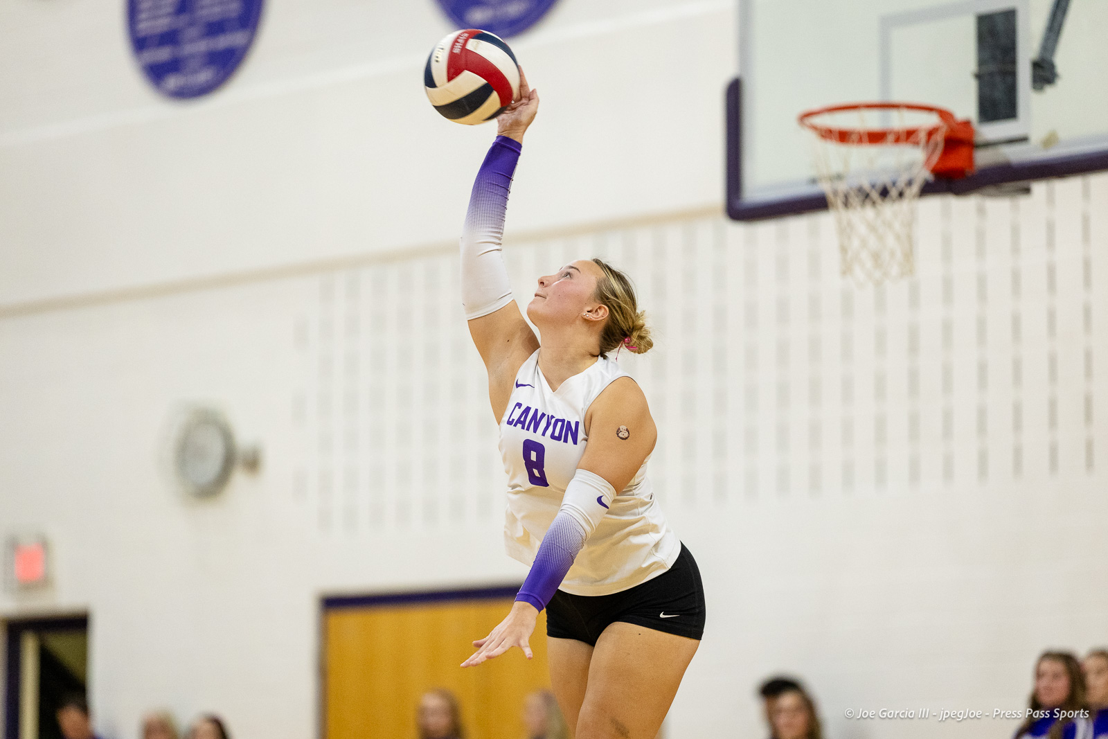 Female volleyball player in a white Canyon jersey (number 8) leaps to spike the ball in a gym.