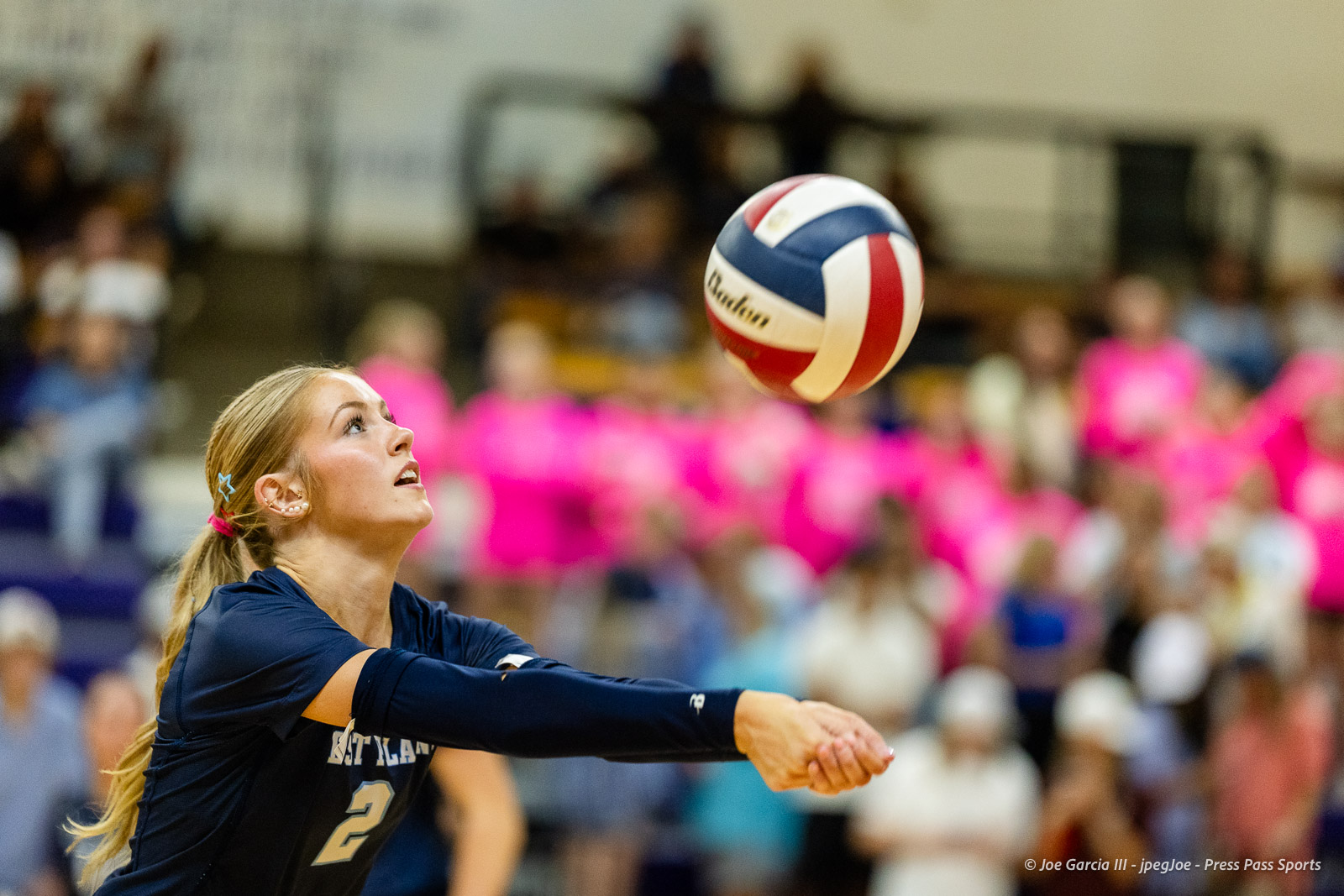 Female volleyball player in a navy jersey reaches to hit a red, white, and blue ball during a match.