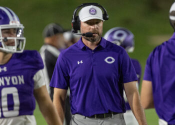 THS-CHS-FB-37 | Press Pass Sports Football coach wearing a purple polo and headset on the sideline during a game at night.