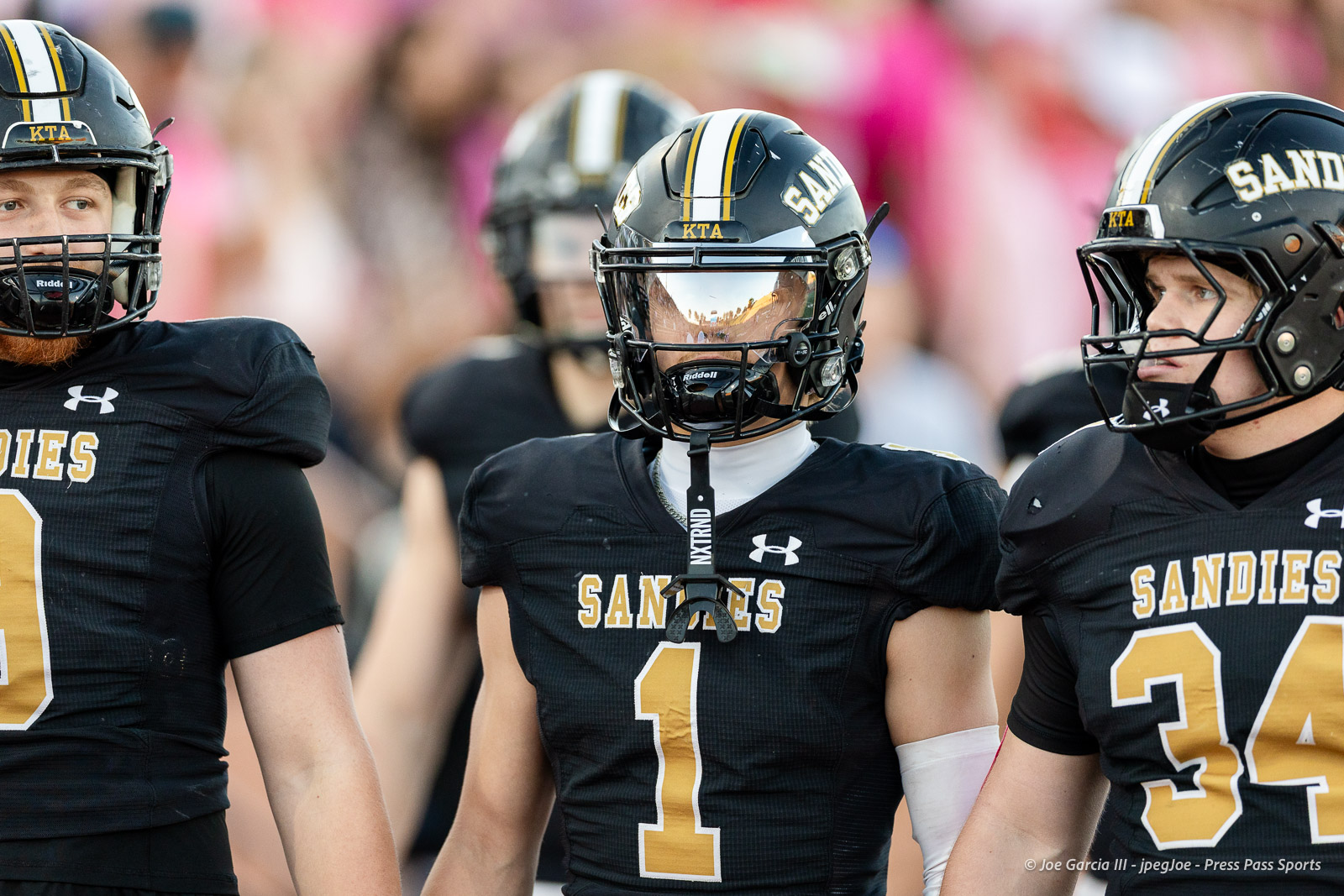 lubbock-monterey-vs-amarillo-high-football-jpegJoe-pps-1 | Press Pass Sports Three Sandies football players in black jerseys with gold numbers stand together on the field, helmets on and a blurred crowd behind them.
