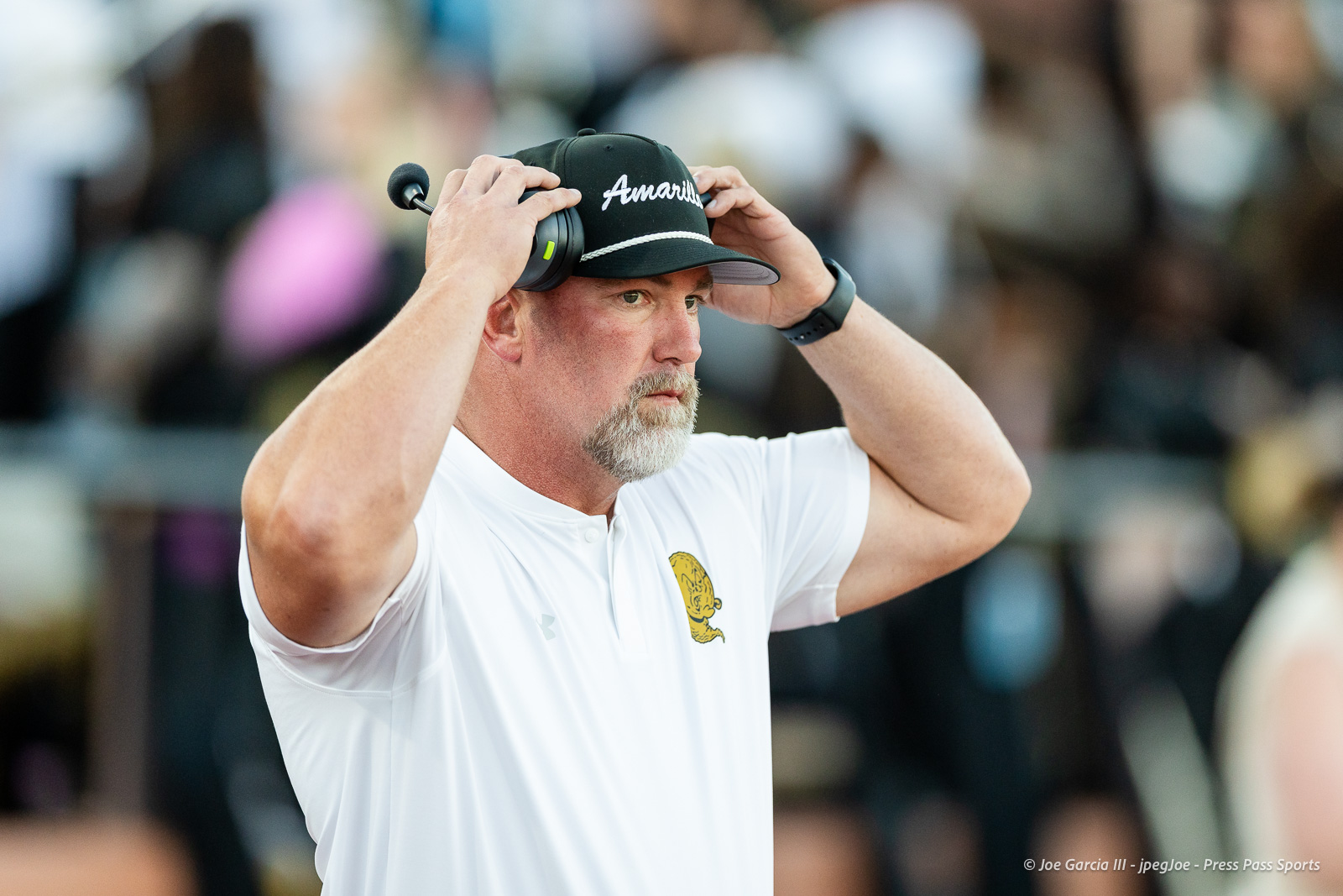 lubbock-monterey-vs-amarillo-high-football-jpegJoe-pps-2 | Press Pass Sports Man wearing a black cap and white polo shirt puts on over-ear headphones at a crowded event.