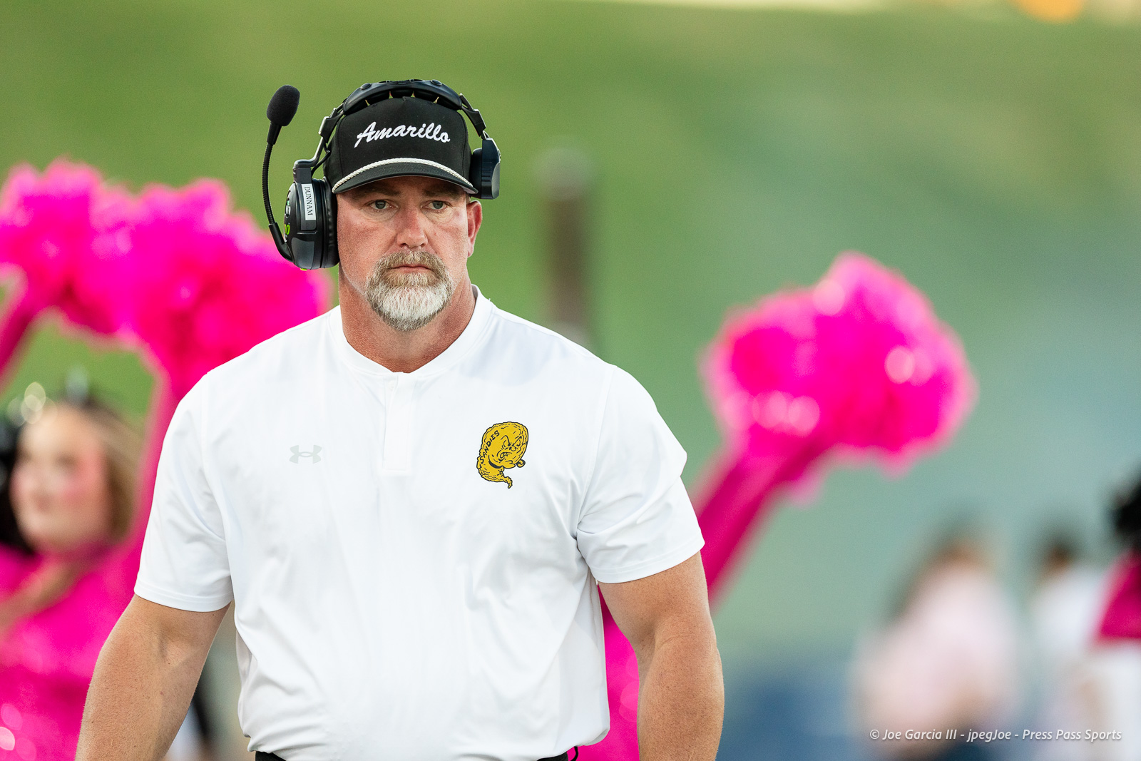 lubbock-monterey-vs-amarillo-high-football-jpegJoe-pps-4 | Press Pass Sports Man wearing a headset and a white polo with a yellow team logo, standing on a sports field outdoors.