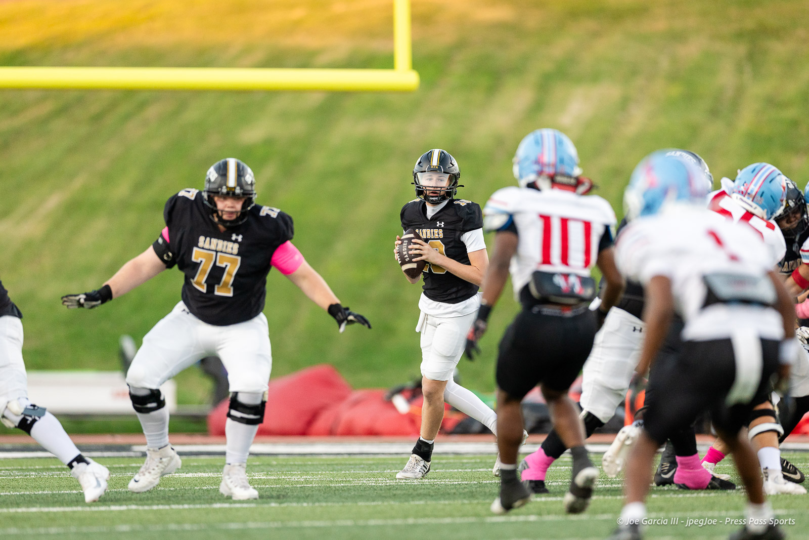 lubbock-monterey-vs-amarillo-high-football-jpegJoe-pps-5 | Press Pass Sports Quarterback in a black jersey holding a football, scanning the field while teammates and opponents move around on the artificial turf football field.