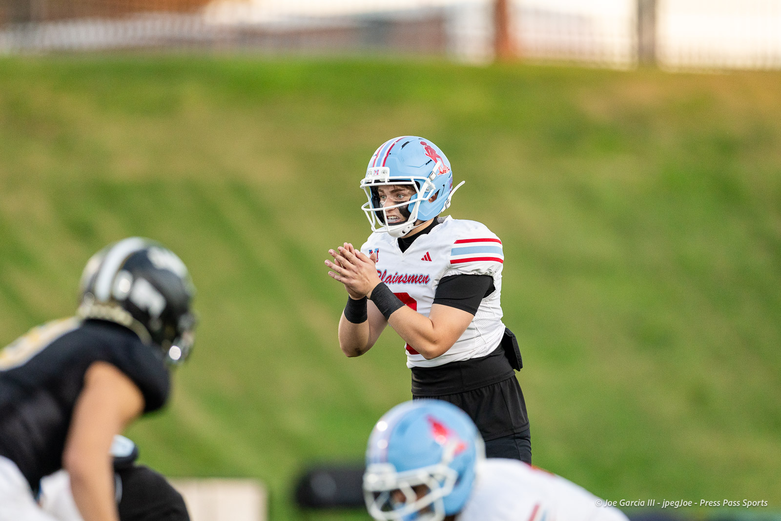 lubbock-monterey-vs-amarillo-high-football-jpegJoe-pps-7 | Press Pass Sports American football scene: a player in a white jersey and blue helmet claps while facing an opposing player in black on a grassy field.