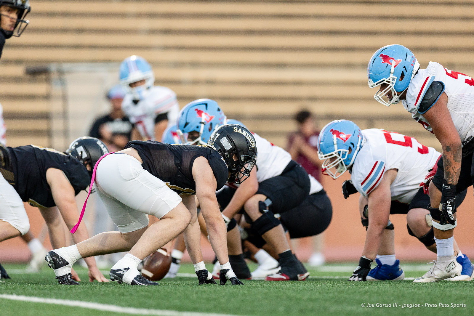 lubbock-monterey-vs-amarillo-high-football-jpegJoe-pps-8 | Press Pass Sports American football players line up at the line of scrimmage on a green field before the snap (center in black, others in white and blue helmets).