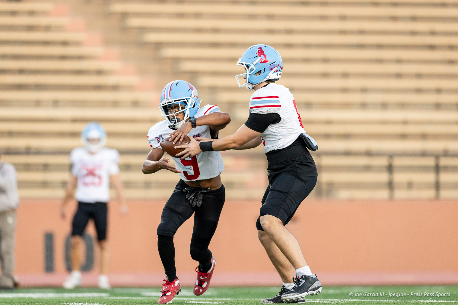 lubbock-monterey-vs-amarillo-high-football-jpegJoe-pps-9 | Press Pass Sports Football players in white jerseys and blue helmets contest a catch during a game on a green field, one grabbing the ball while another reaches in.
