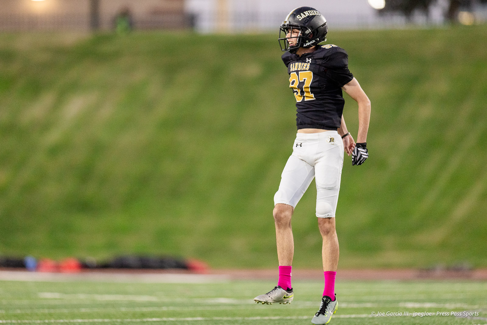 lubbock-monterey-vs-amarillo-high-football-jpegJoe-pps-12 | Press Pass Sports Football player in black uniform with number 37 standing on a grassy field, pink socks, wearing a helmet and gloves.