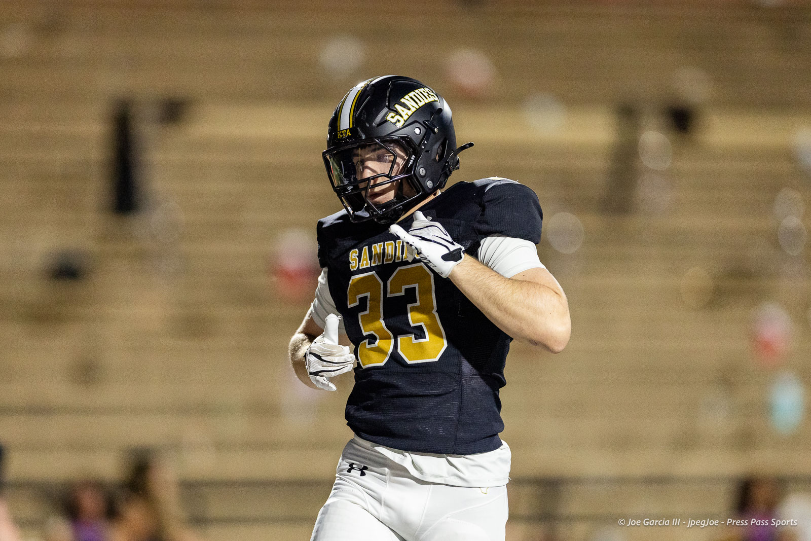 lubbock-monterey-vs-amarillo-high-football-jpegJoe-pps-19 | Press Pass Sports Football player wearing a black jersey with number 33 and a Sandites helmet runs on an indoor field, white pants and gloves visible.