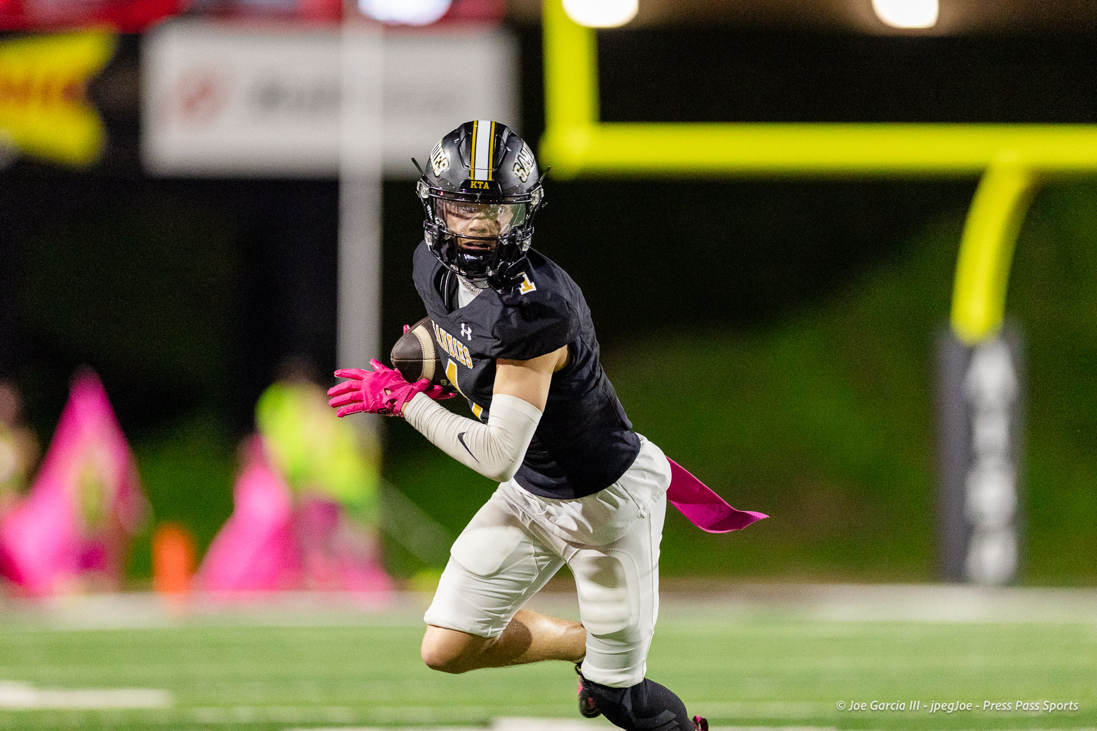 lubbock-monterey-vs-amarillo-high-football-jpegJoe-pps-21 | Press Pass Sports Football player in a black uniform with pink gloves runs with the ball on a night game, yellow goalposts in the background.