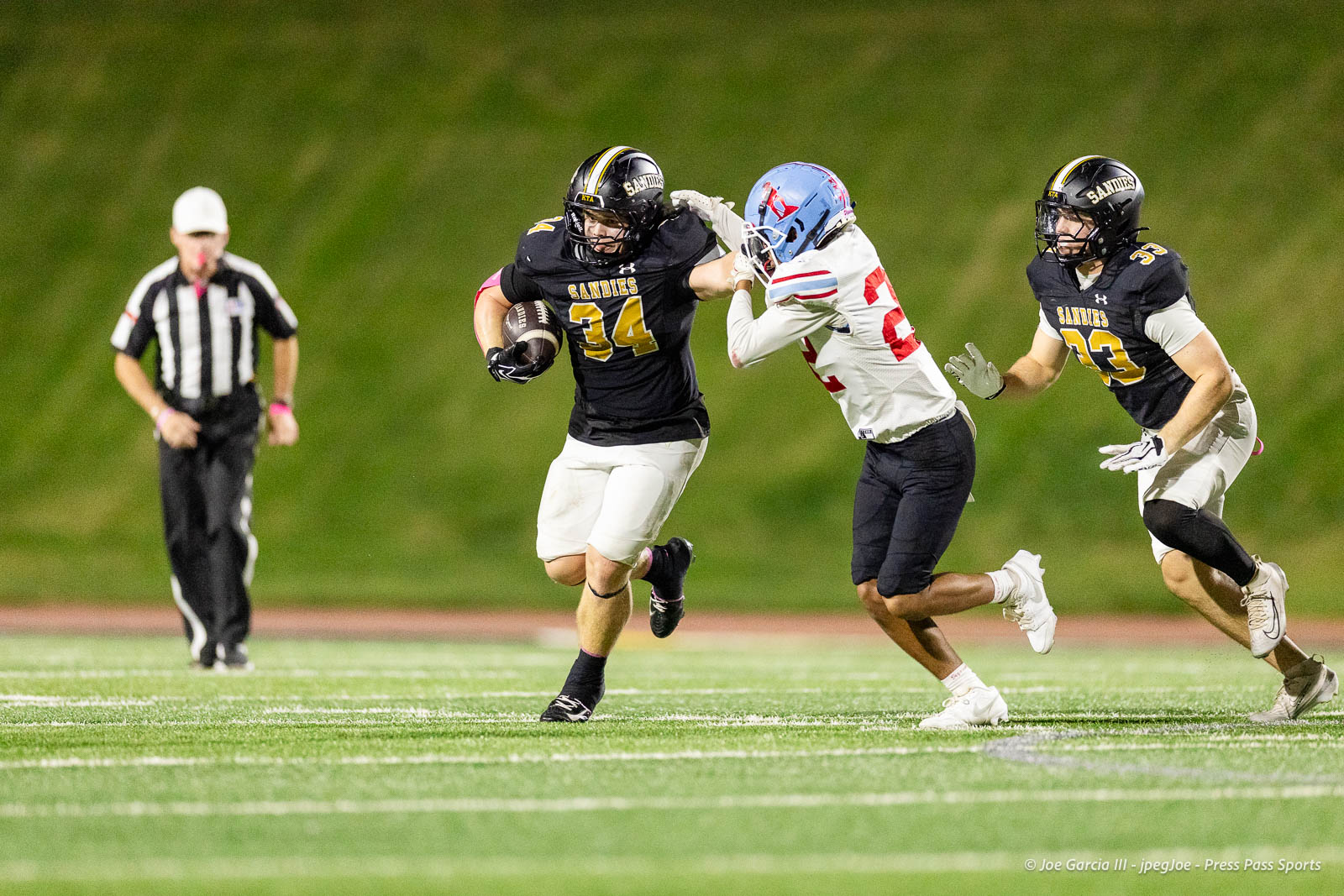lubbock-monterey-vs-amarillo-high-football-jpegJoe-pps-27 | Press Pass Sports Sandies running back #34 carries the ball while a defender in white pursues him on a green football field at night.