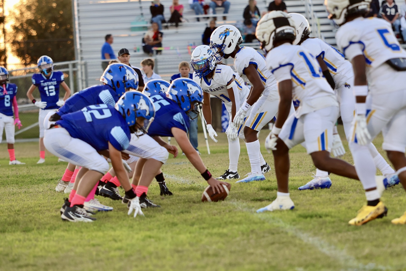 Line of scrimmage in a youth football game: blue team on offense faces white team on defense with players crouched and ready to snap the ball.