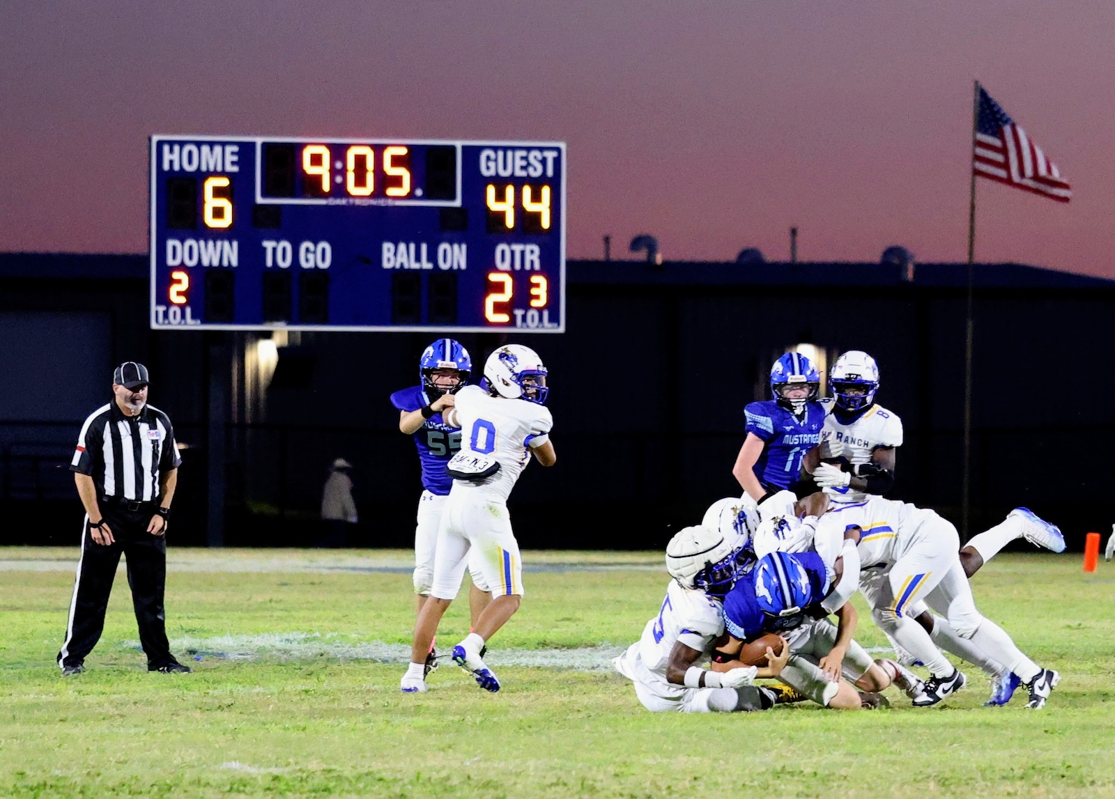 Football action: players pile up and tackle near the ball on a grassy field as the scoreboard reads Home 6, Guest 44, 9:05 left out of 4th.