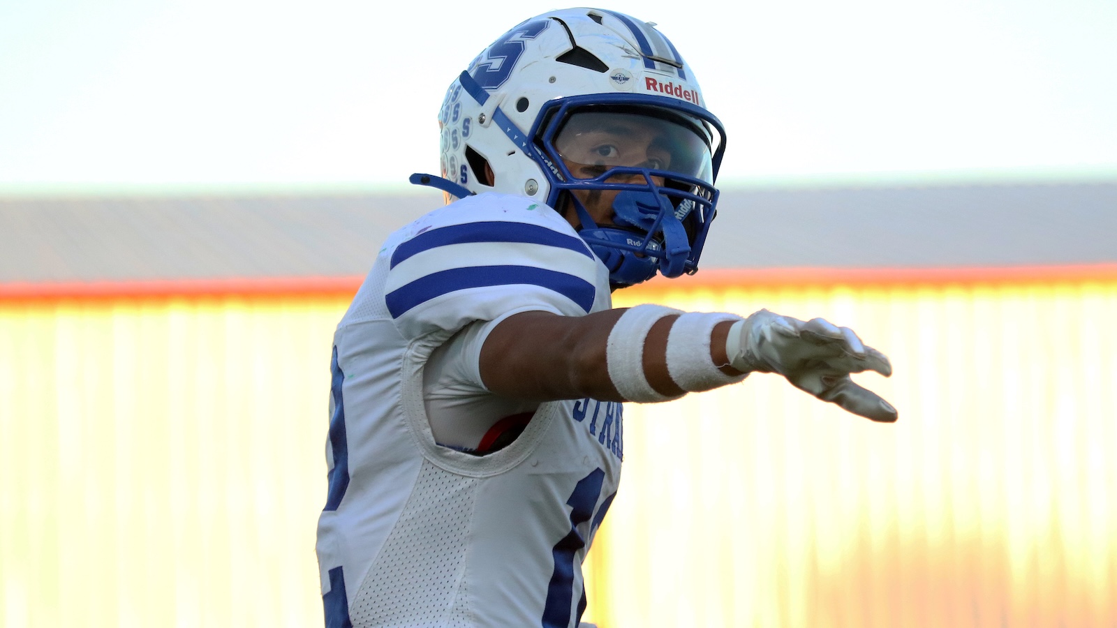 Football player in a white and blue uniform extends his right arm during a play, wearing a white helmet with a blue faceguard.