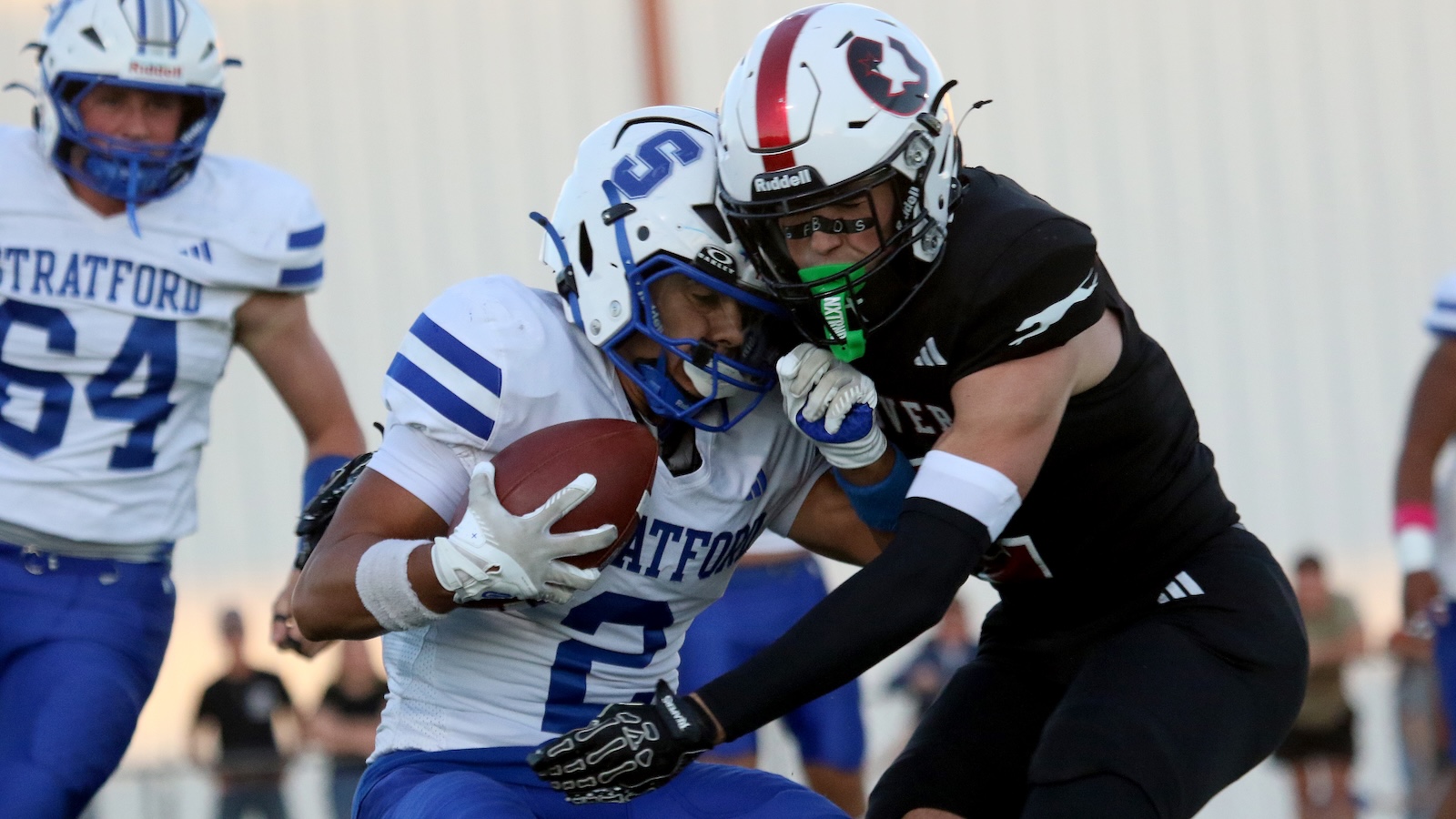 Football action: a Stratford player in white and blue runs with the ball while a defender in black reaches to tackle him.