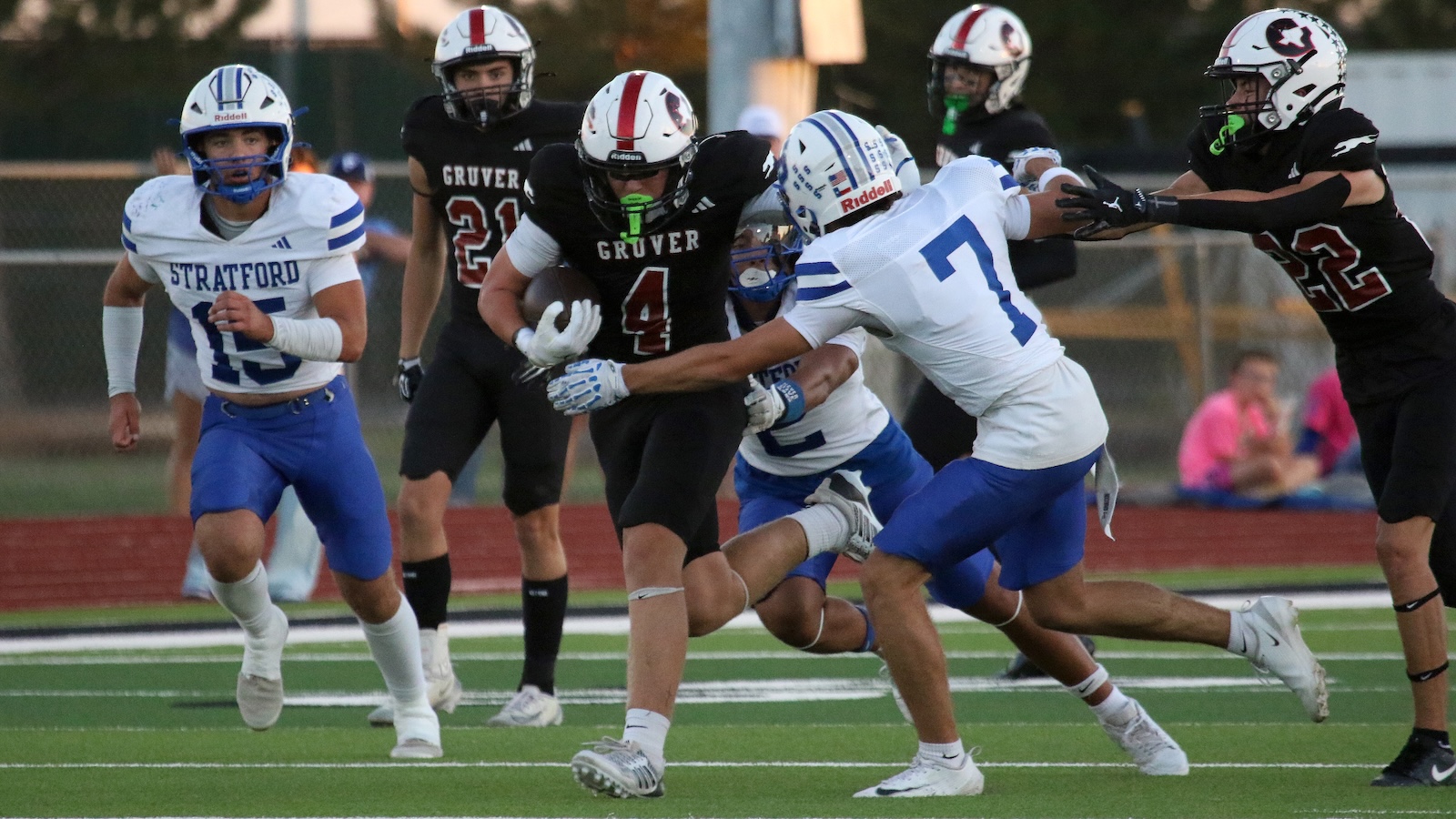 High school football scene: Grover #4 runs with the ball as Stratford players in white and blue close in for a tackle on a green turf field.