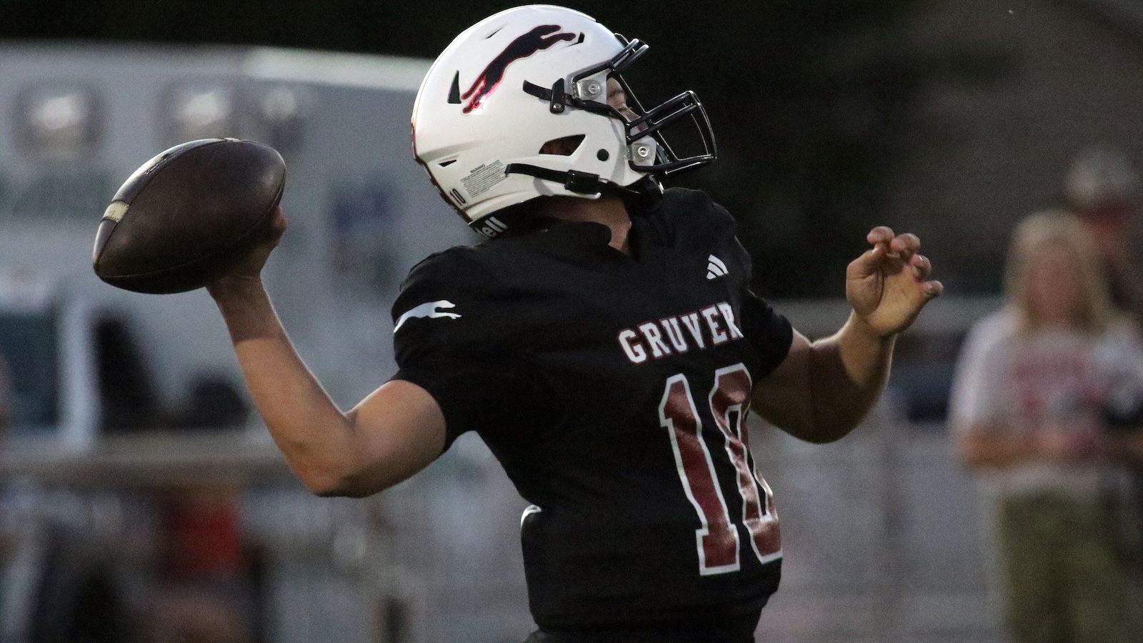 Football player in a black jersey (#11) with'GRIVER' on the back, mid-throw as he launches a football during a game.