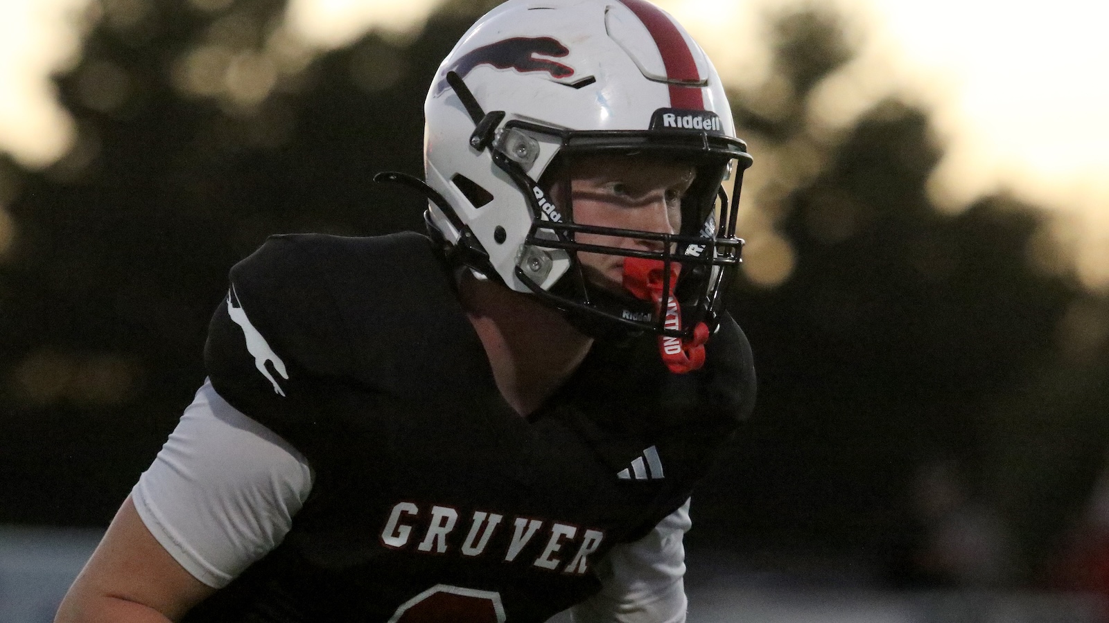 Football player in black jersey (CRUVER) and white helmet on the field, focused and ready for action at dusk.