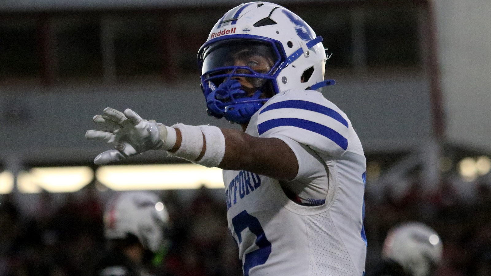 Football player in a white and blue uniform extends his arm during a game.