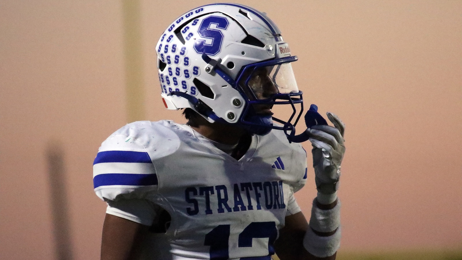 Football player in a white and blue Stratford jersey #13, wearing a white helmet with blue S logo, adjusting his facemask in profile.