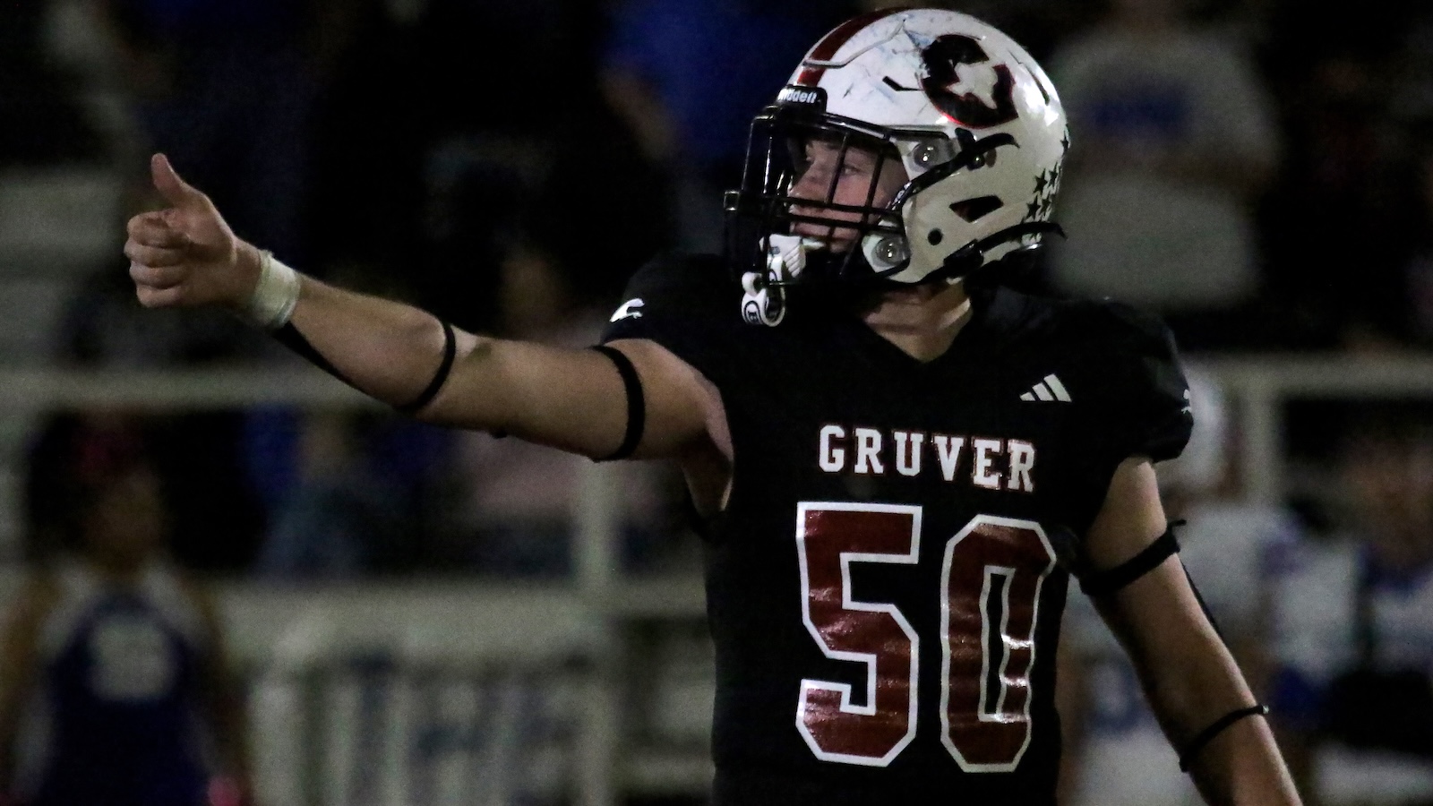 Football player in a black Gruver jersey #50 points to the left with his arm extended during a game at night.