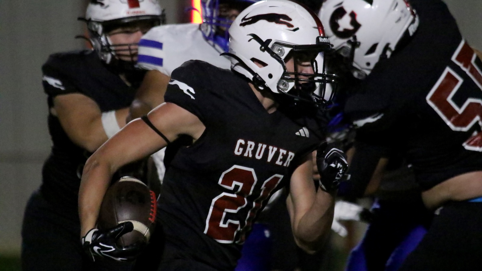 Gruver football player #21 runs with ball during a night game, wearing a white helmet and black jersey.