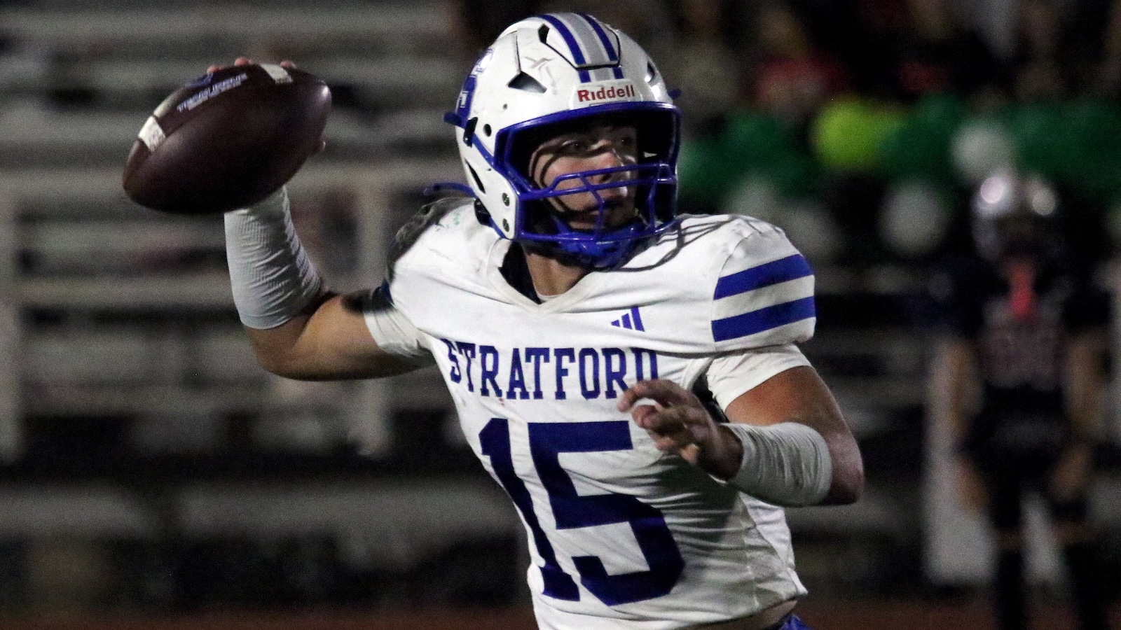 Stratford football quarterback in white and purple throwing a pass under stadium lights (number 15).