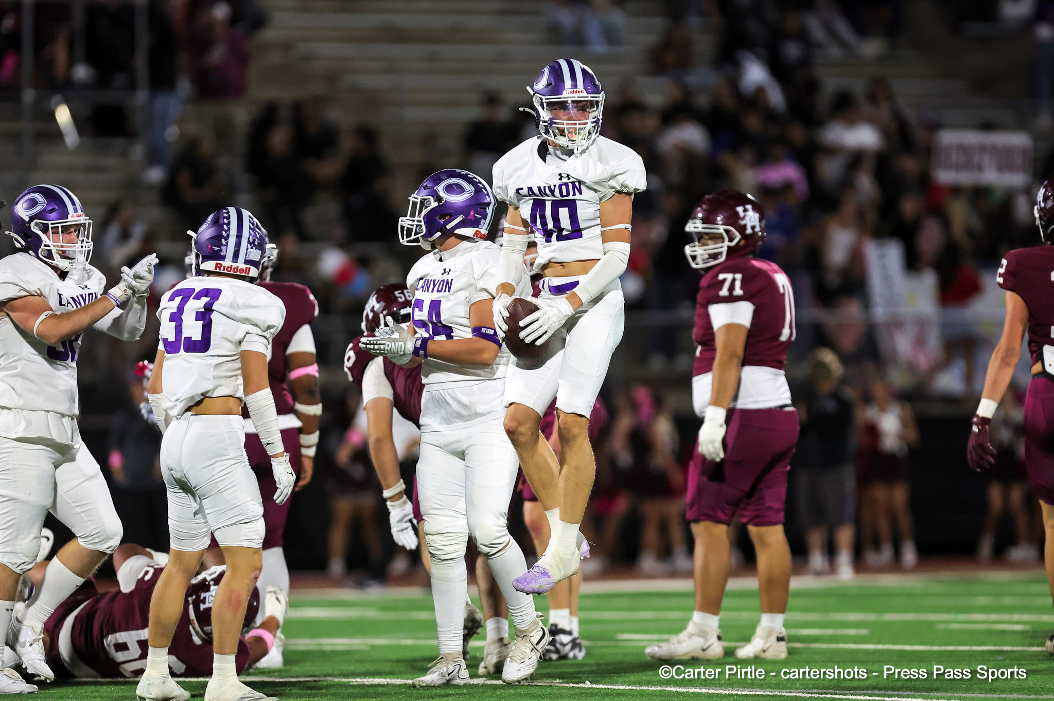 Canyon football player in white jersey (#40) leaps with the ball while teammates and opponents surround him on the field at night.