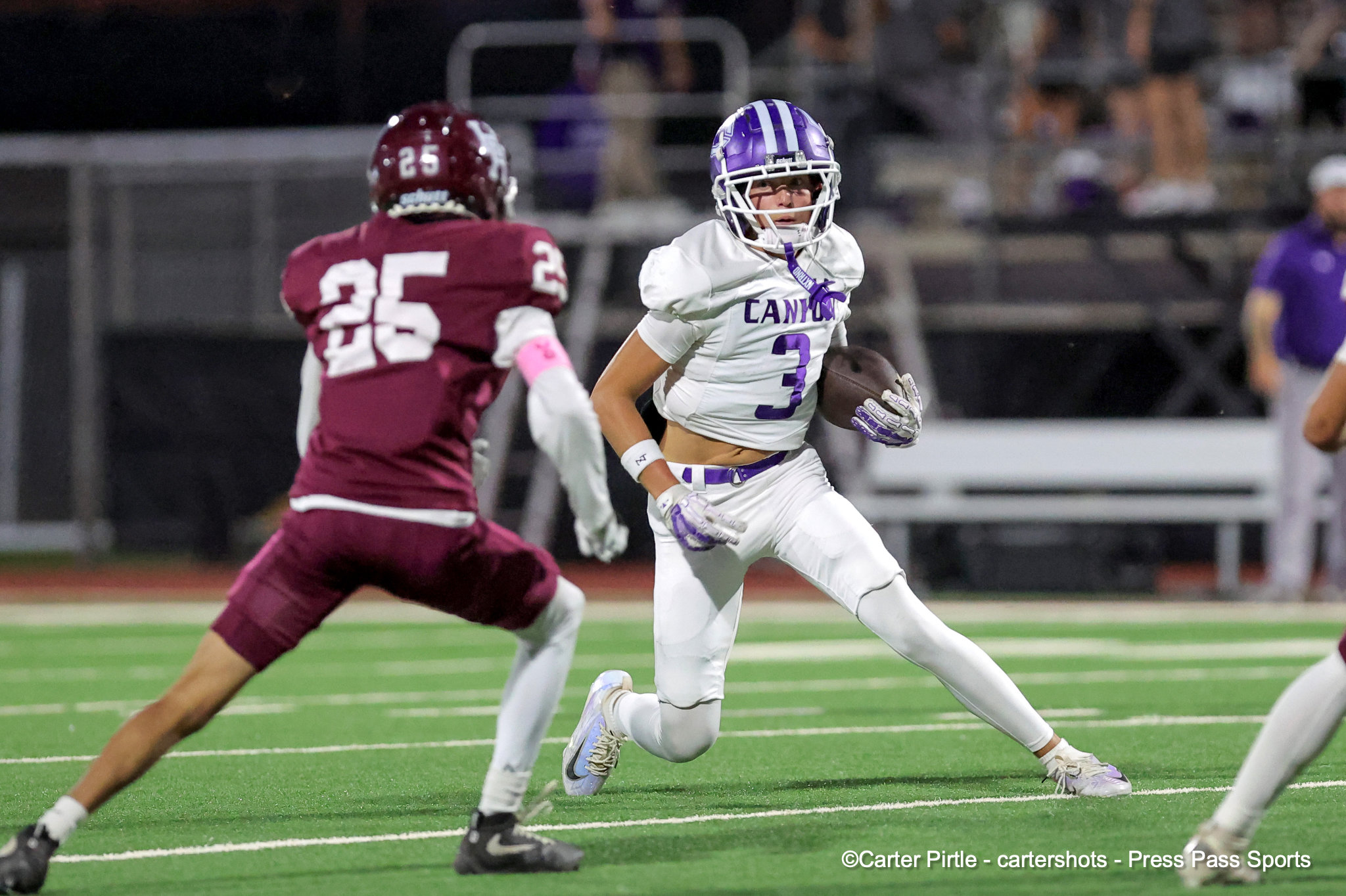 Running back in white and purple with ball, sprinting downfield as a defender in maroon chases him.
