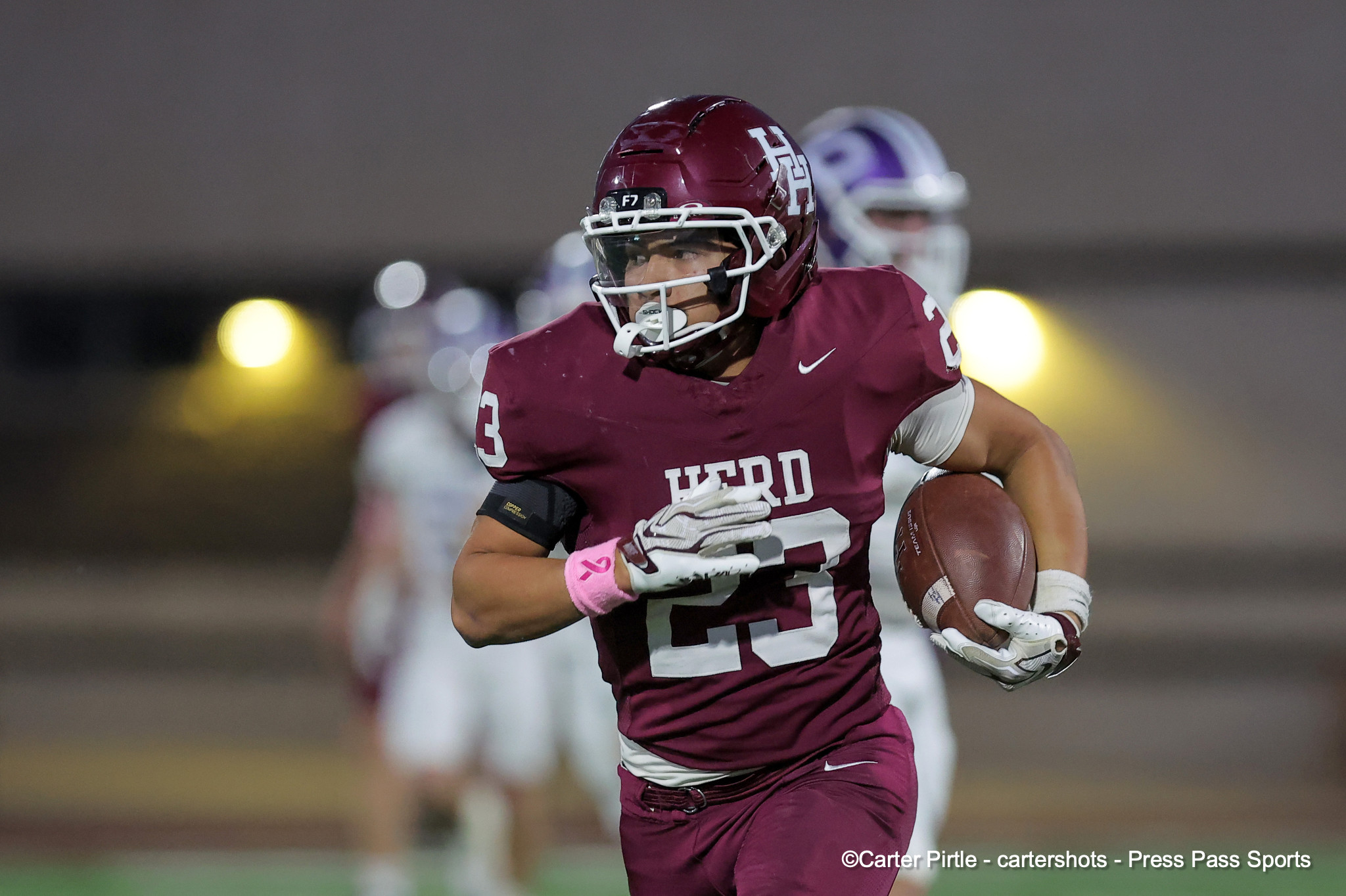 Football player in a maroon uniform runs with the ball during a night game, helmet on and focus forward.