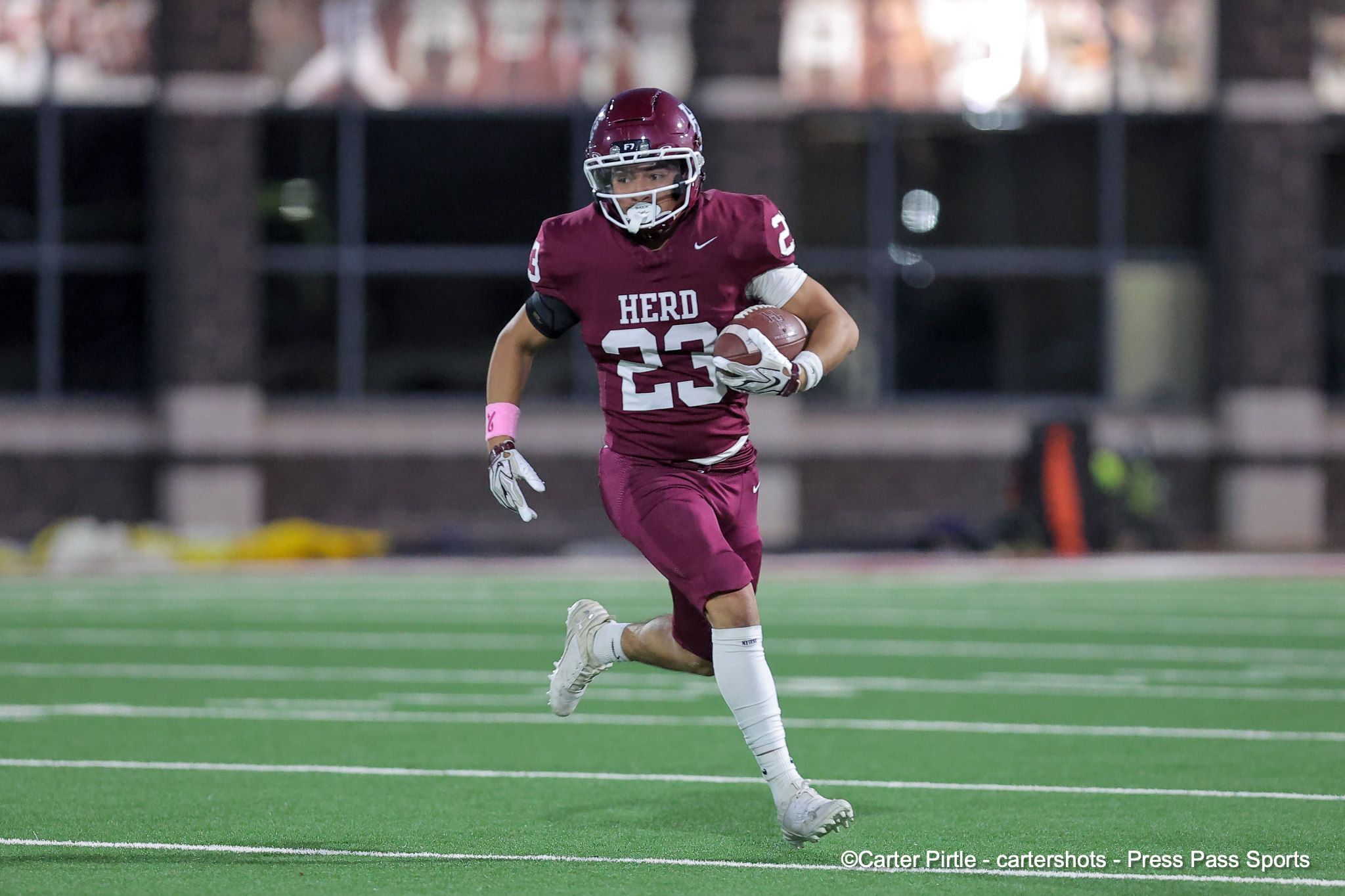 Herd football player wearing number 23 in maroon runs with the ball on a green field during a game