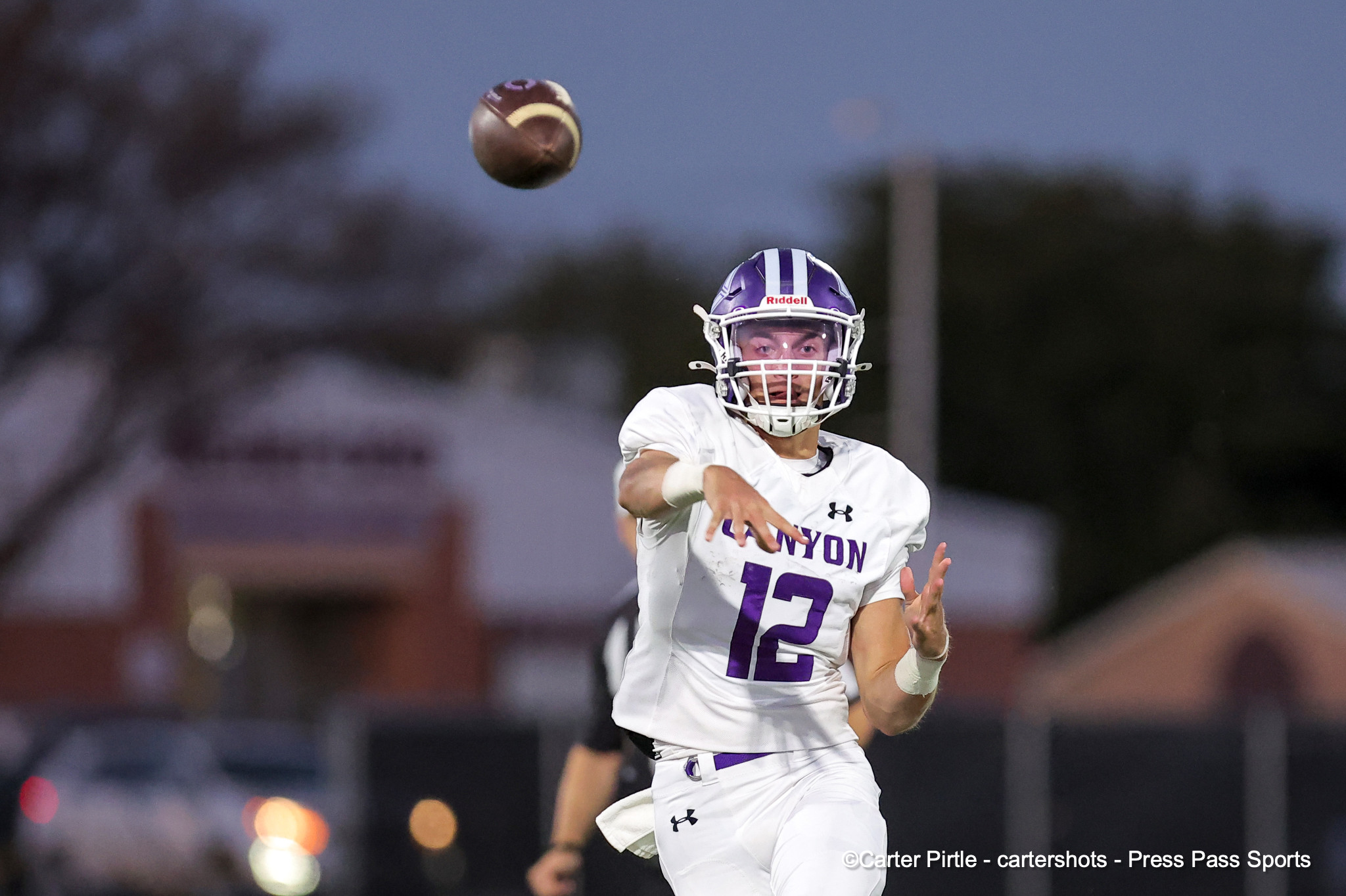 Football player in white and purple uniform reaching for a high football during a night game under stadium lights.