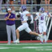 20261009-Canyon-Hereford-FB-015 | Press Pass Sports Football players in white and purple uniforms on the sidelines; player 25 runs with the ball while a teammate (#16) cheers"