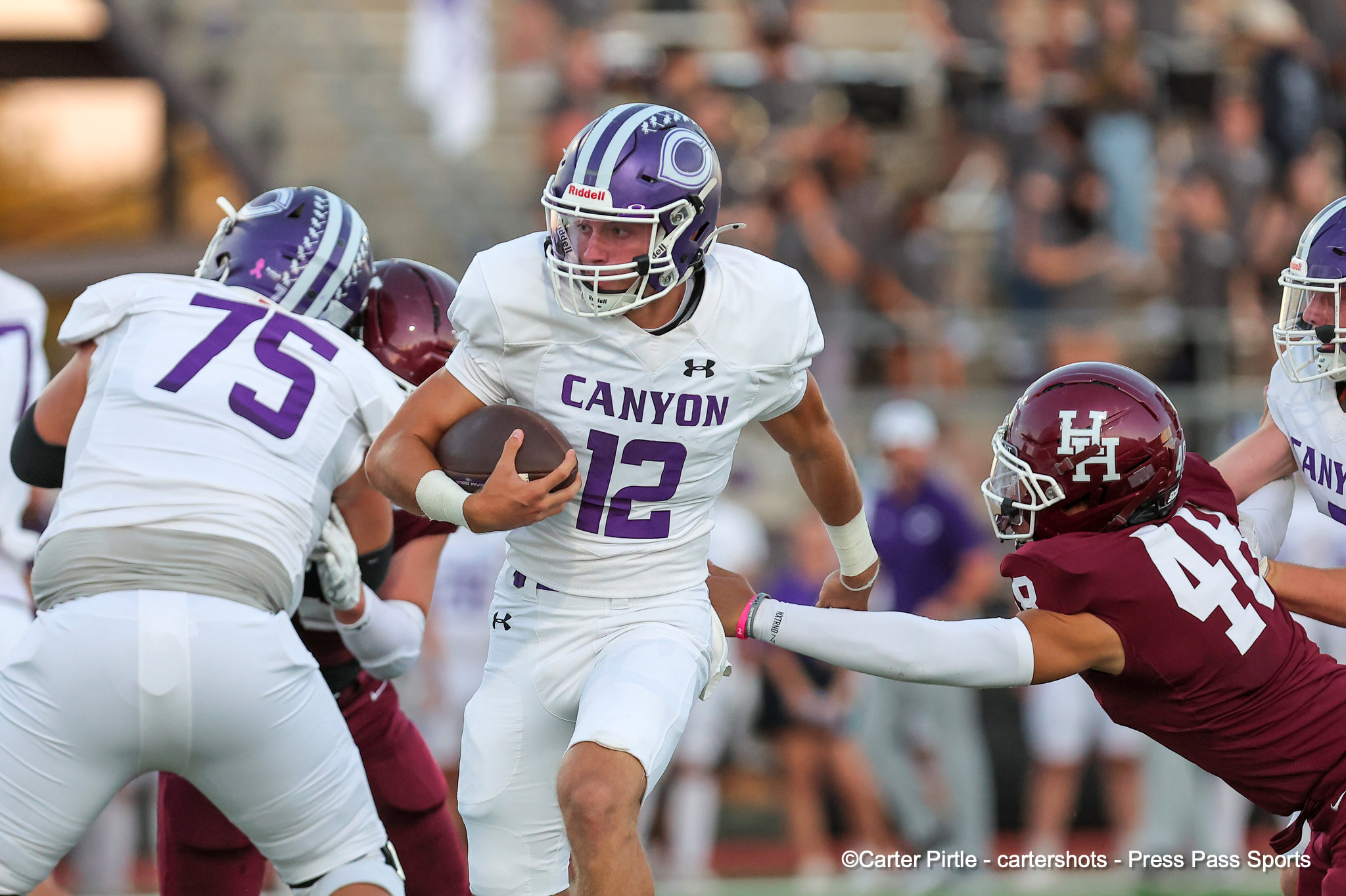 Canyon quarterback wearing #12 in white runs with the ball as defenders converge in a high-action football play