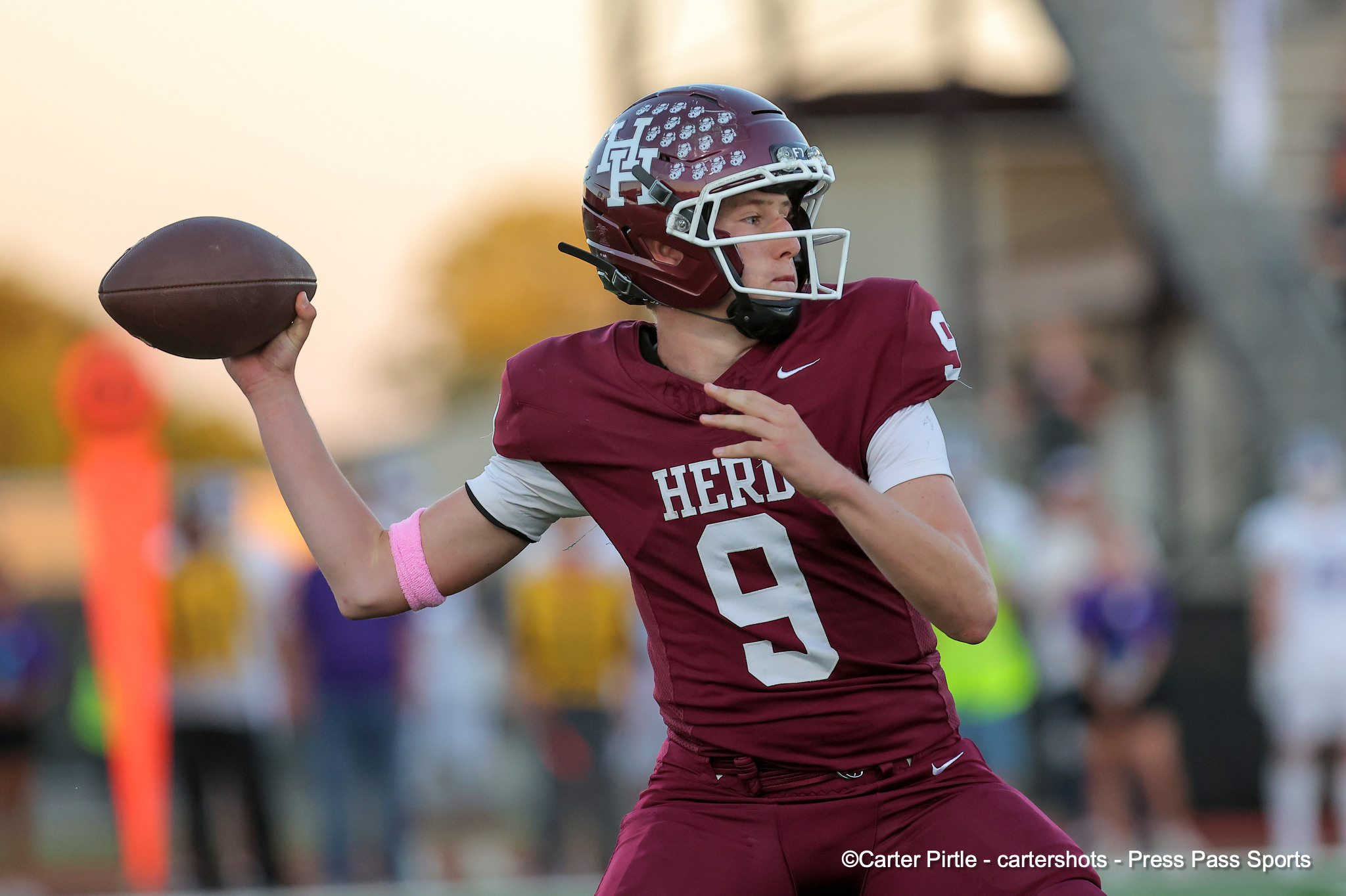 Quarterback in maroon uniform throwing a pass during a football game with white facemask helmet