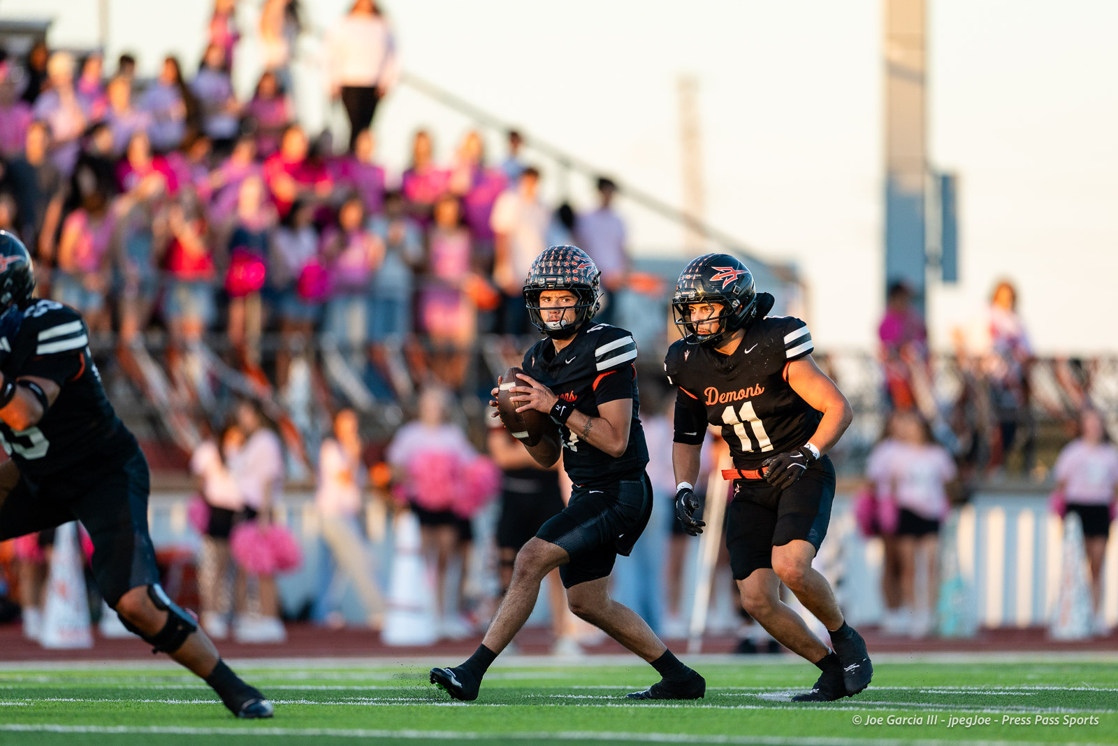 west-plains-vs-dumas-football-jpegJoe-pps-1 | Press Pass Sports Two football players in black Demons uniforms sprint on a turf field, crowd in stands blurred behind them.