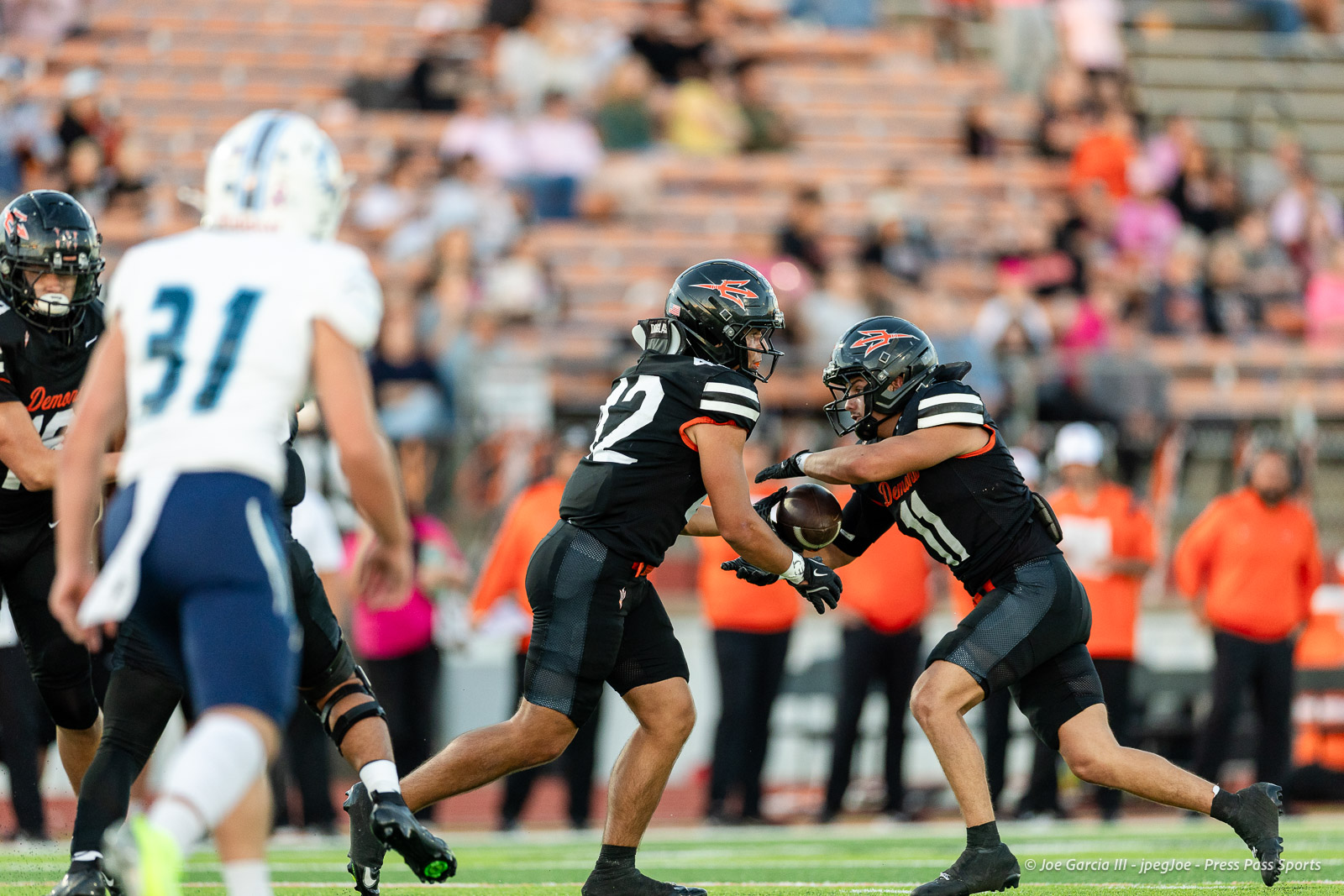 west-plains-vs-dumas-football-jpegJoe-pps-2 | Press Pass Sports Football players in black uniforms converge as one guards the ball while another reaches for a tackle on the field; white-clad opponent approaches in foreground.