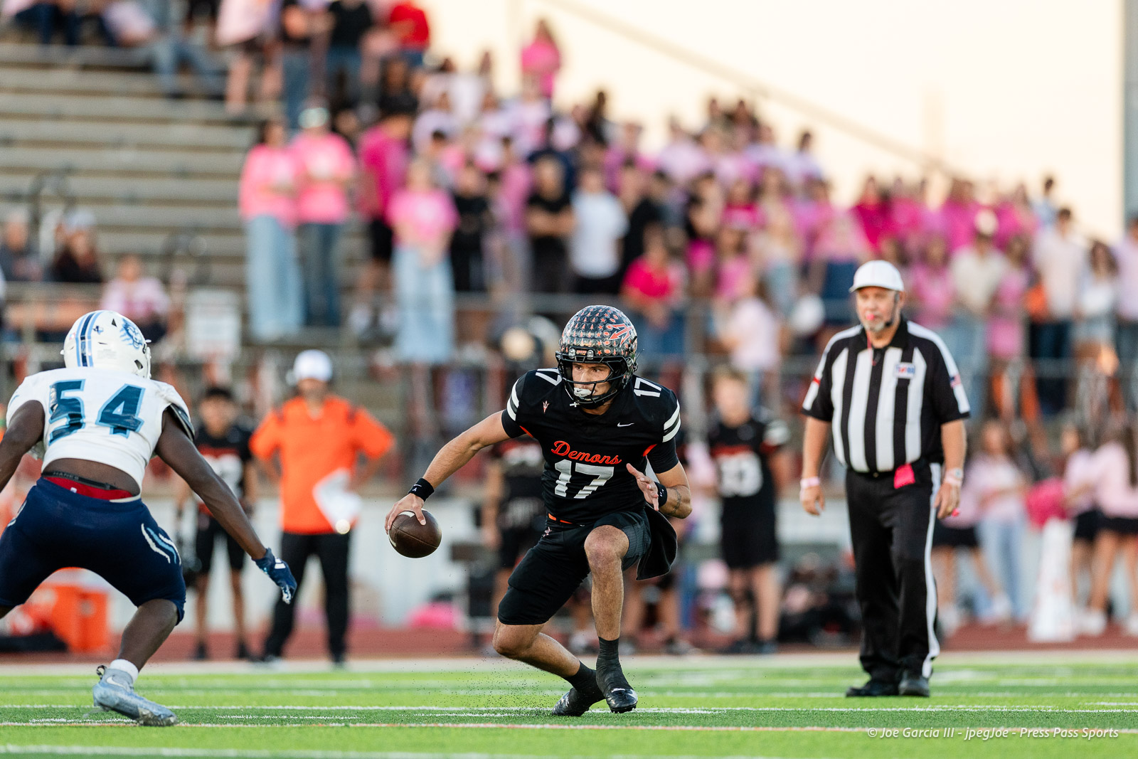 west-plains-vs-dumas-football-jpegJoe-pps-3 | Press Pass Sports Football player in black'Demons' jersey carrying ball, sprinting toward the left as a defender pursues on a green turf field.