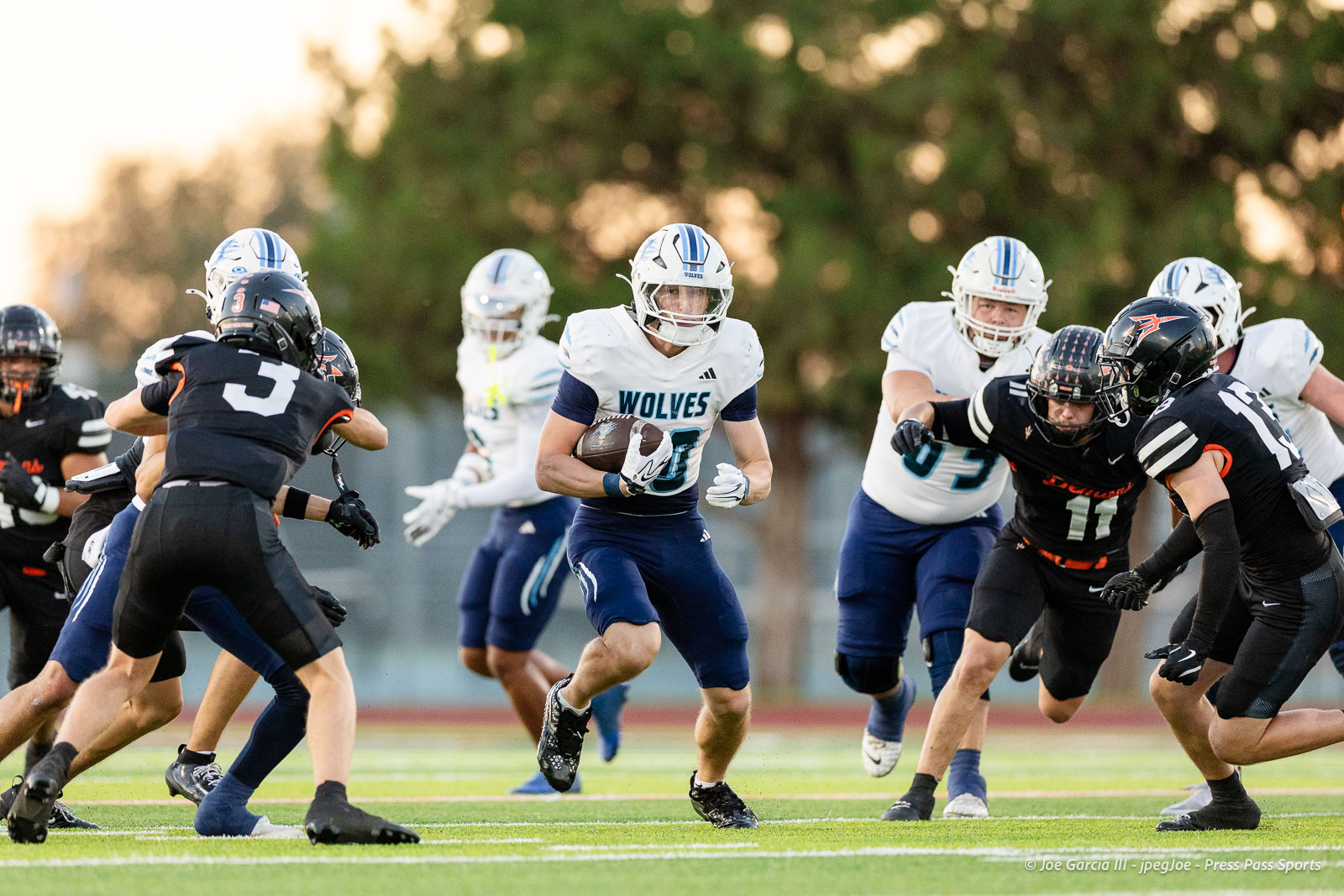 west-plains-vs-dumas-football-jpegJoe-pps-5 | Press Pass Sports Wolves player in white jersey and blue pants runs with the football as defenders close in on both sides on a sunny field.