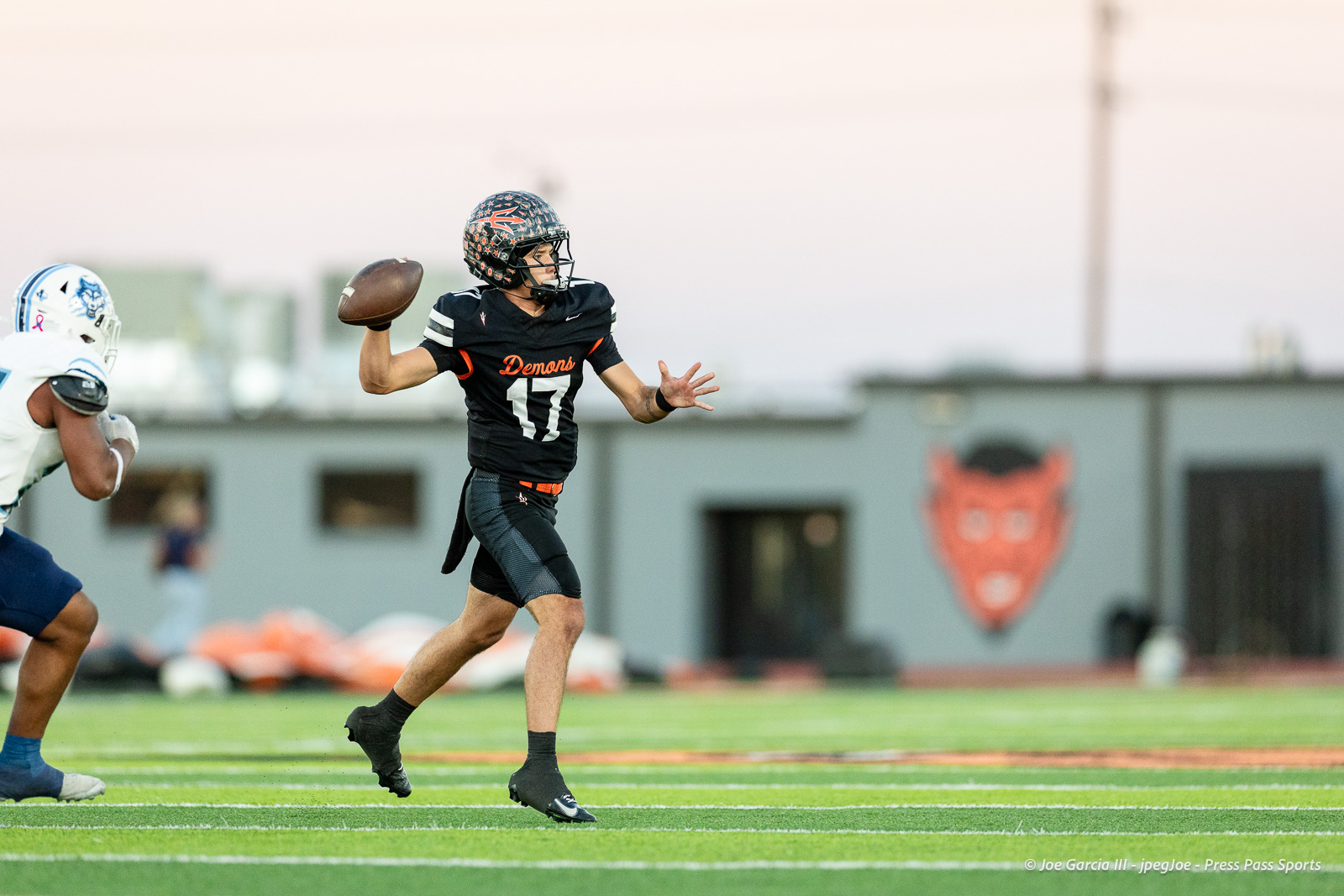 west-plains-vs-dumas-football-jpegJoe-pps-7 | Press Pass Sports Quarterback in a black Demons jersey (number 17) throws a football downfield during a game on a green turf field. nearby defender approaches.