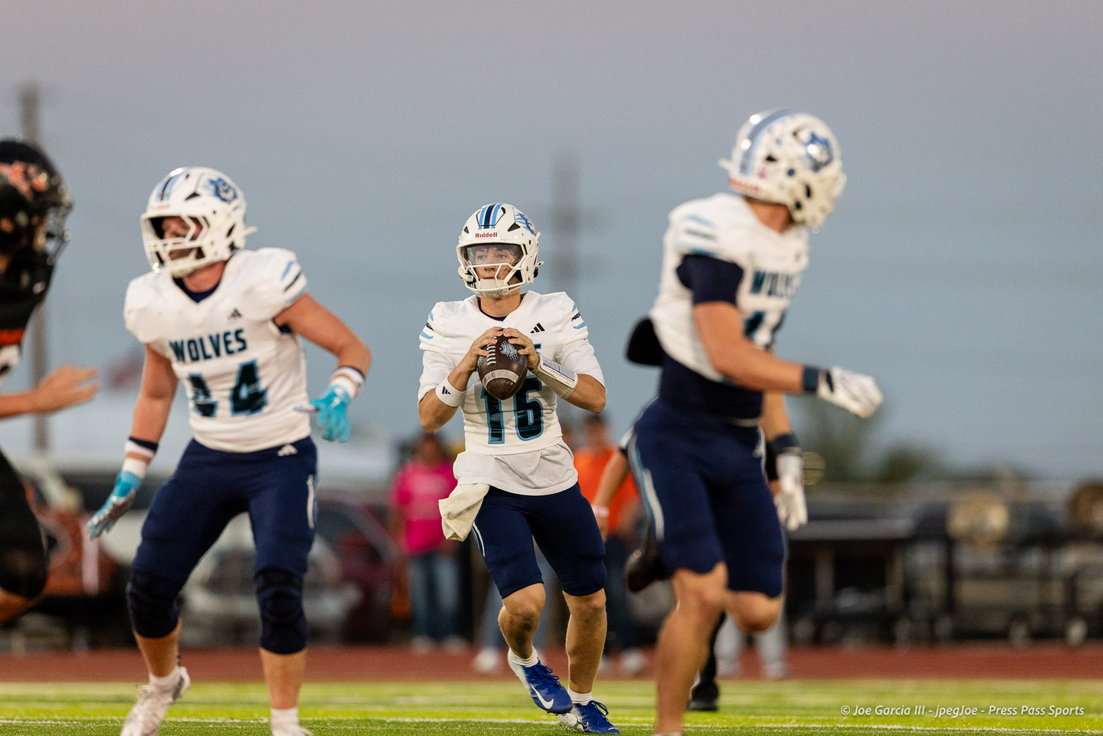 west-plains-vs-dumas-football-jpegJoe-pps-9 | Press Pass Sports Youth football quarterback in white and blue, number 16, winding up to throw a pass on a sunny field with teammates nearby.