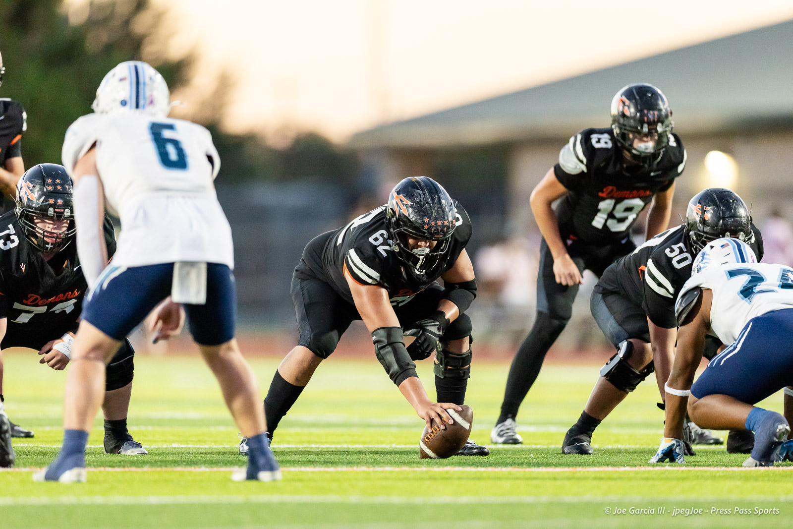 west-plains-vs-dumas-football-jpegJoe-pps-15 | Press Pass Sports American football players at the line of scrimmage; a black-uniform center grips the ball as teammates prepare to snap.
