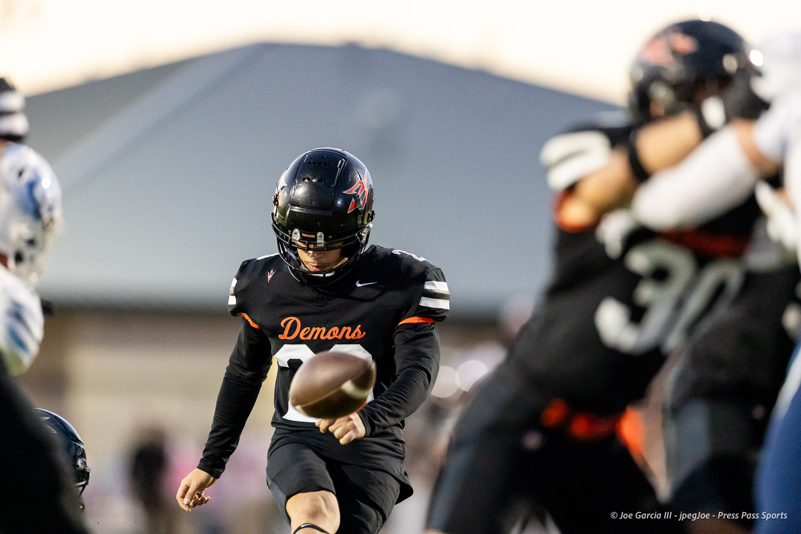 west-plains-vs-dumas-football-jpegJoe-pps-16 | Press Pass Sports Football player in a black Demons uniform reaching for a ball mid‑play as defenders stand nearby.