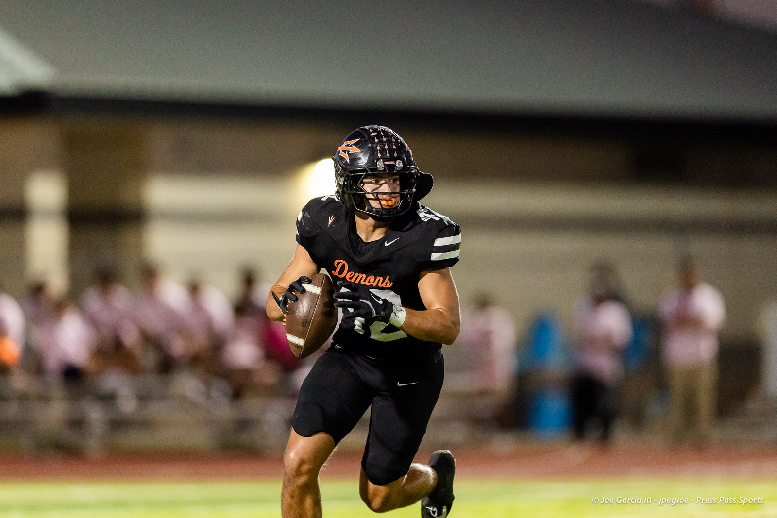 west-plains-vs-dumas-football-jpegJoe-pps-21 | Press Pass Sports Football player in a black Demons uniform runs with the ball on a football field, with a blurred crowd in the background.