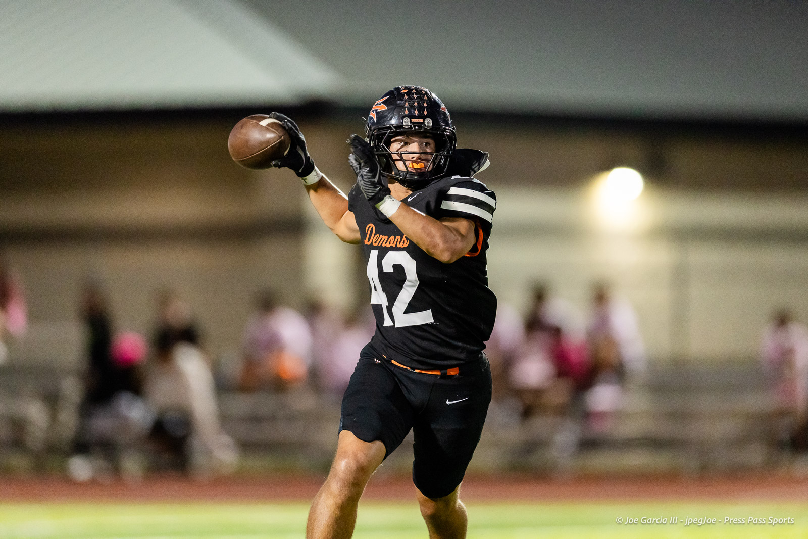 west-plains-vs-dumas-football-jpegJoe-pps-22 | Press Pass Sports Quarterback in a black Demons jersey (#42) throwing a pass on a lit football field with a blurred crowd in the background